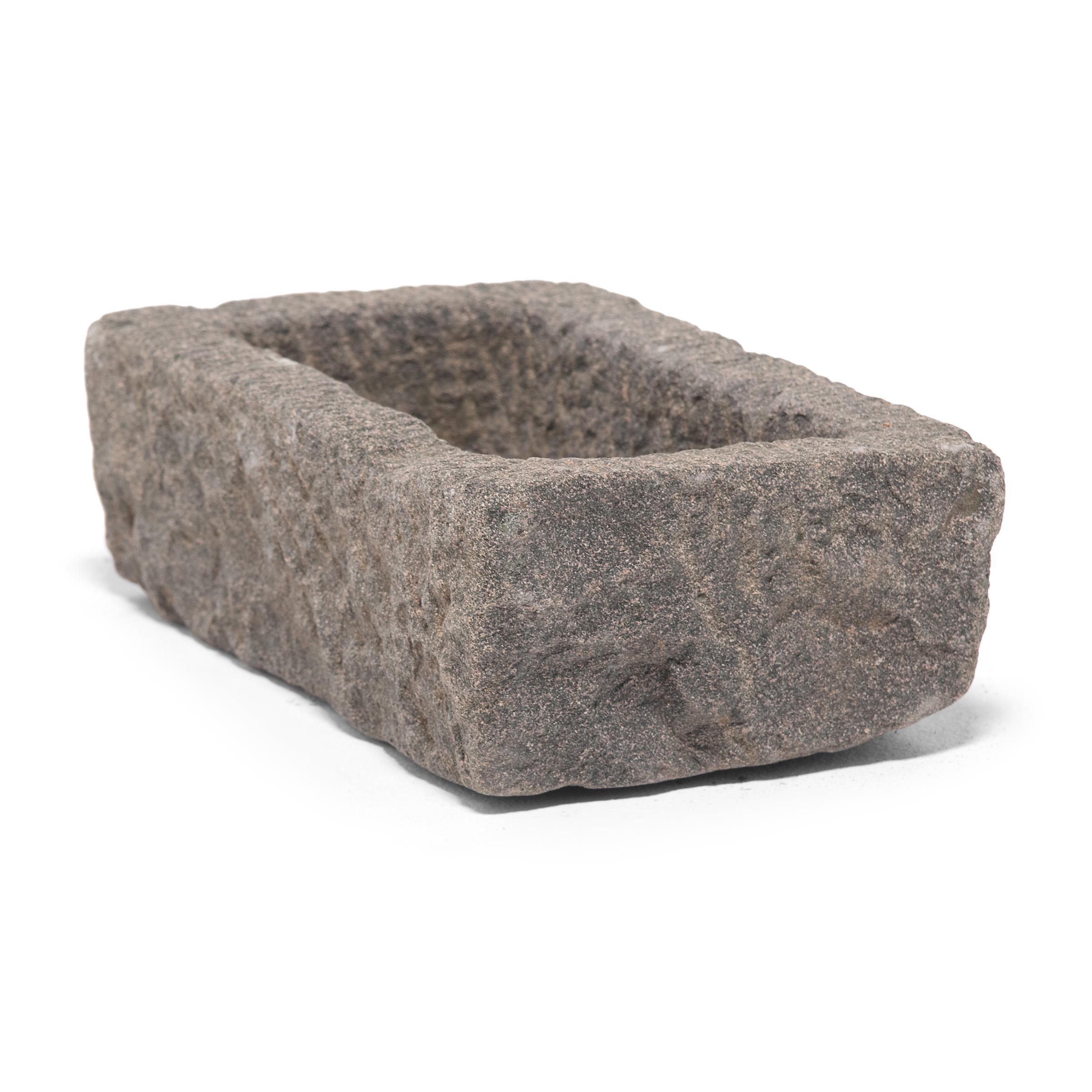 Once a common sight in courtyards throughout rural China, this textured stone vessel was used as a grain trough for chickens and other barnyard fowl. Chiseled from a block of granite over a century ago, the sculptural trough charms with its uneven