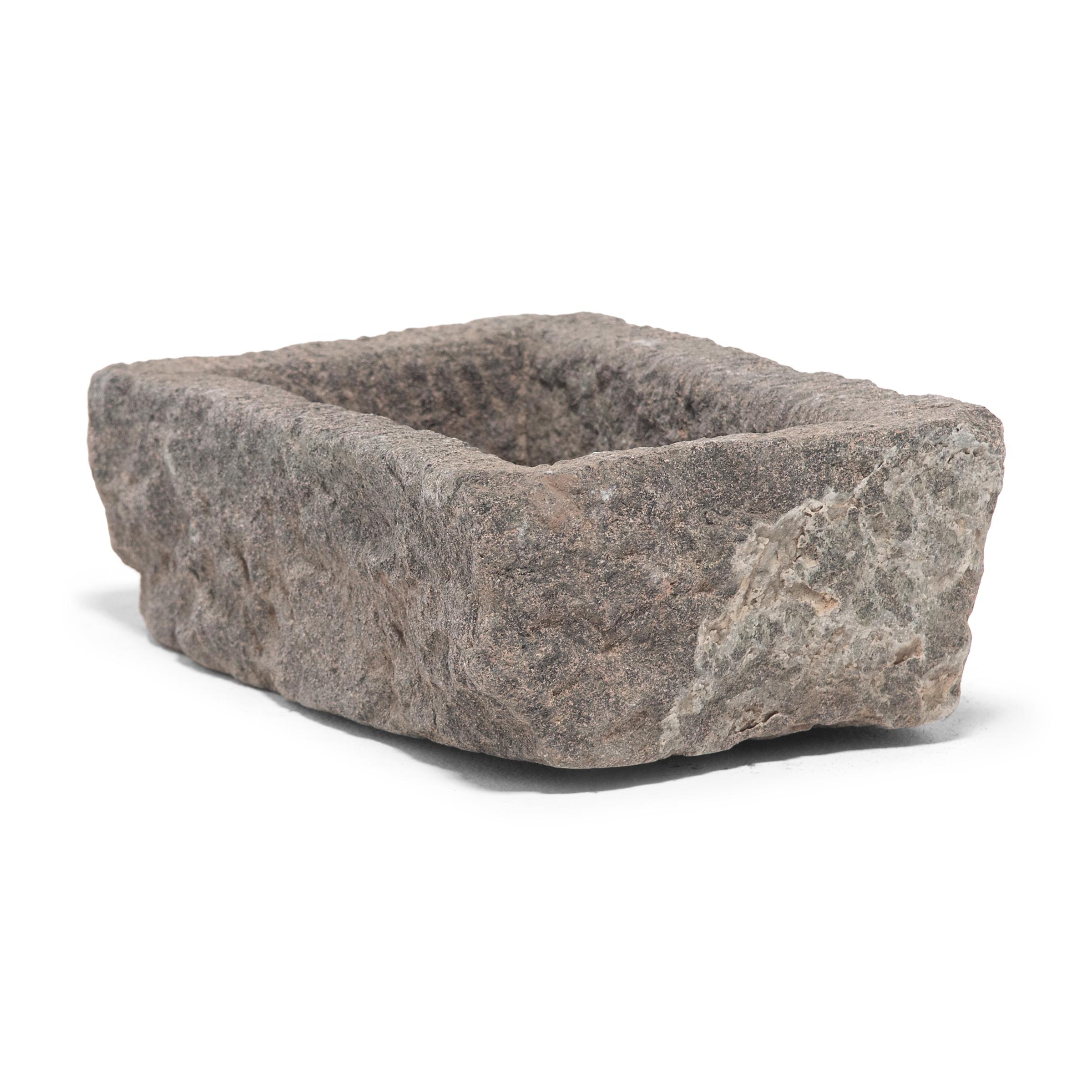 Once a common sight in courtyards throughout rural China, this textured stone vessel was used as a grain trough for chickens and other barnyard fowl. Chiseled from a block of granite over a century ago, the sculptural trough charms with its uneven