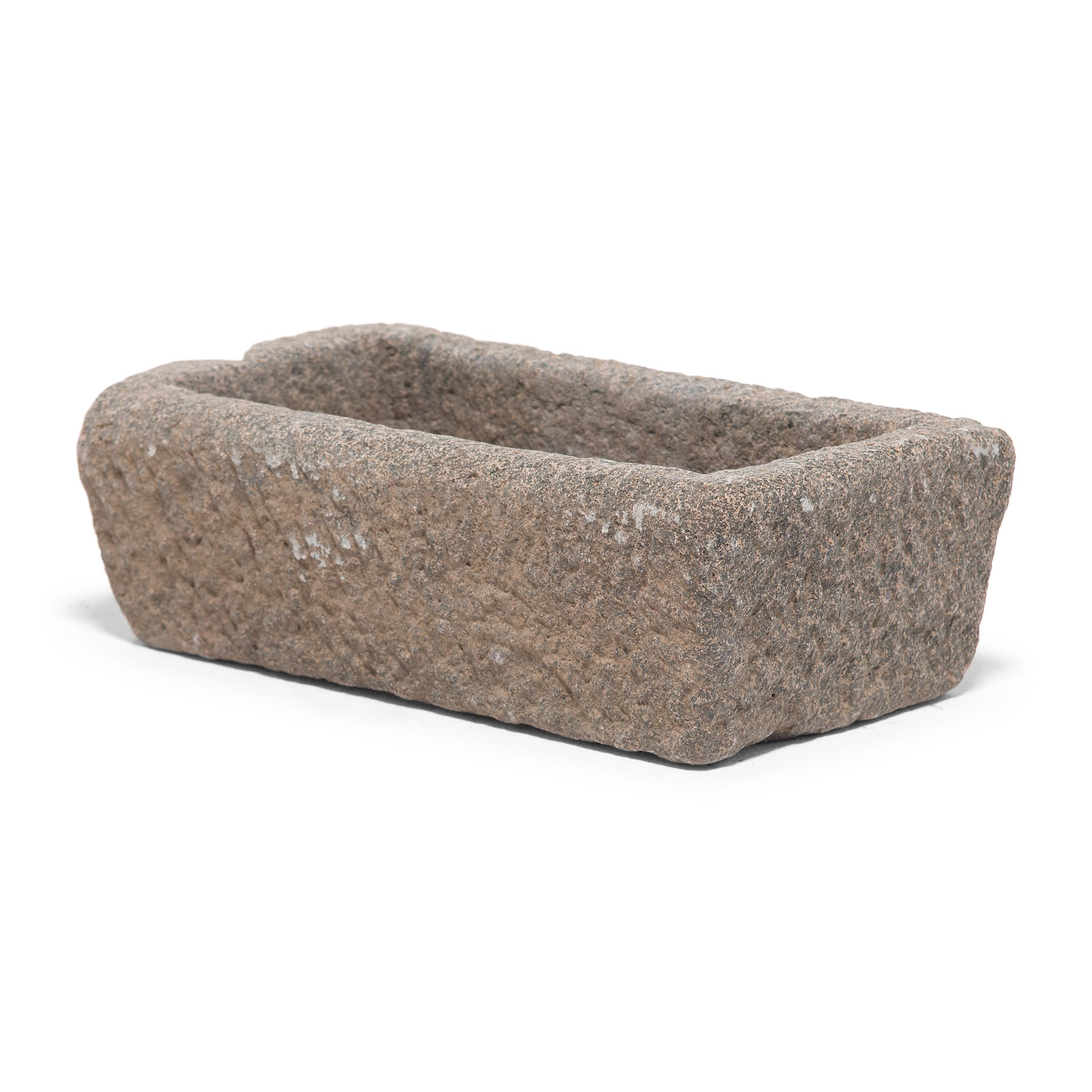 Once a common sight in courtyards throughout rural China, this textured stone vessel was used as a grain trough for chickens and other barnyard fowl. Chiseled from a block of granite over a century ago, the sculptural trough charms with its uneven