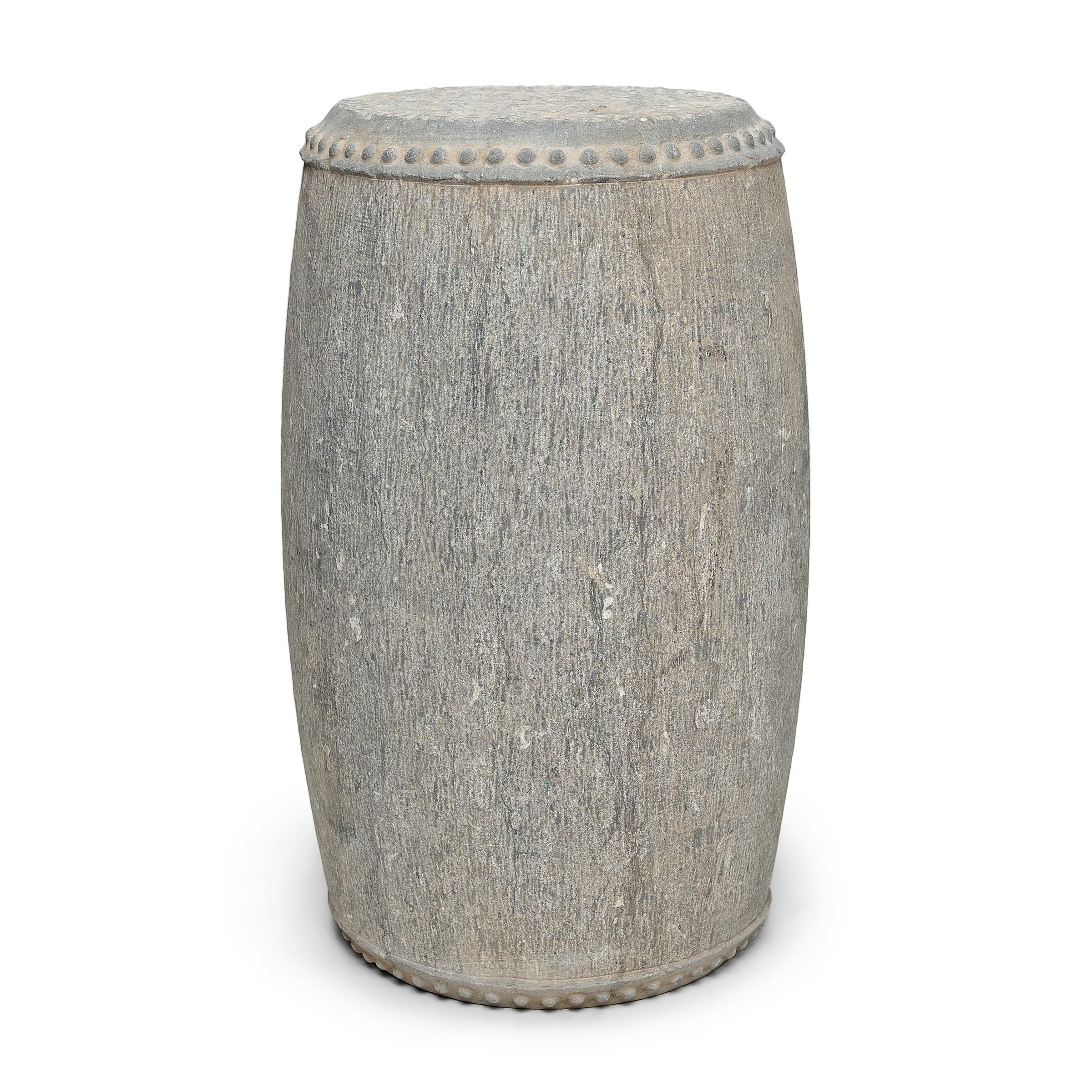 Ce tabouret tambour élancé en pierre a été sculpté dans un bloc massif de calcaire avec une forme simple et une décoration minimale. Le dessus et le dessous sont cerclés de clous en relief, un motif destiné à imiter les rivets en fer qui fixent la