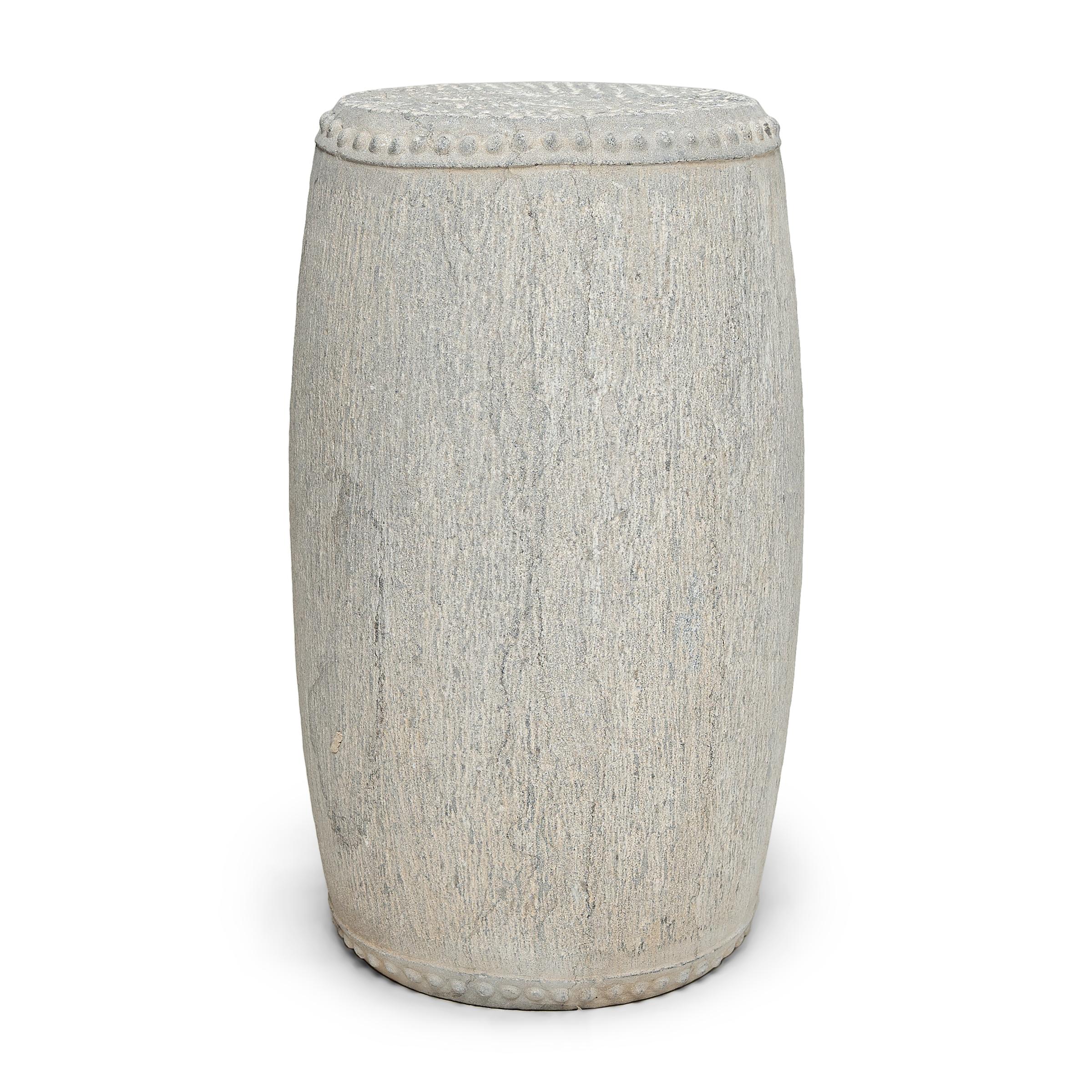 This slender stone drum stool was carved from a solid block of limestone with simple form and minimal decoration. The top and bottom are ringed with raised studs, a design meant to imitate the iron rivets that fasten stretched hide across a drum