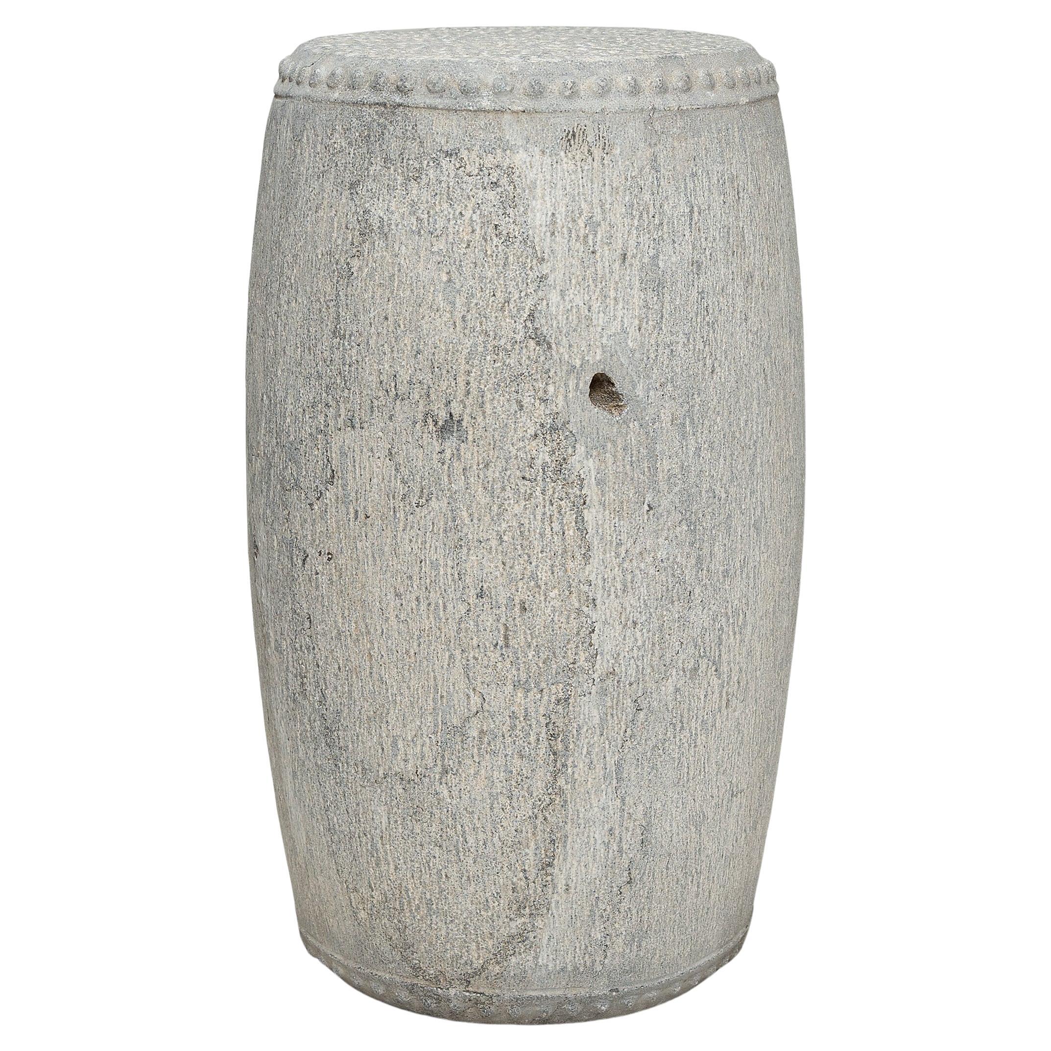 This slender stone drum stool was carved from a solid block of limestone with simple form and minimal decoration. The top and bottom are ringed with raised studs, a design meant to imitate the iron rivets that fasten stretched hide across a drum