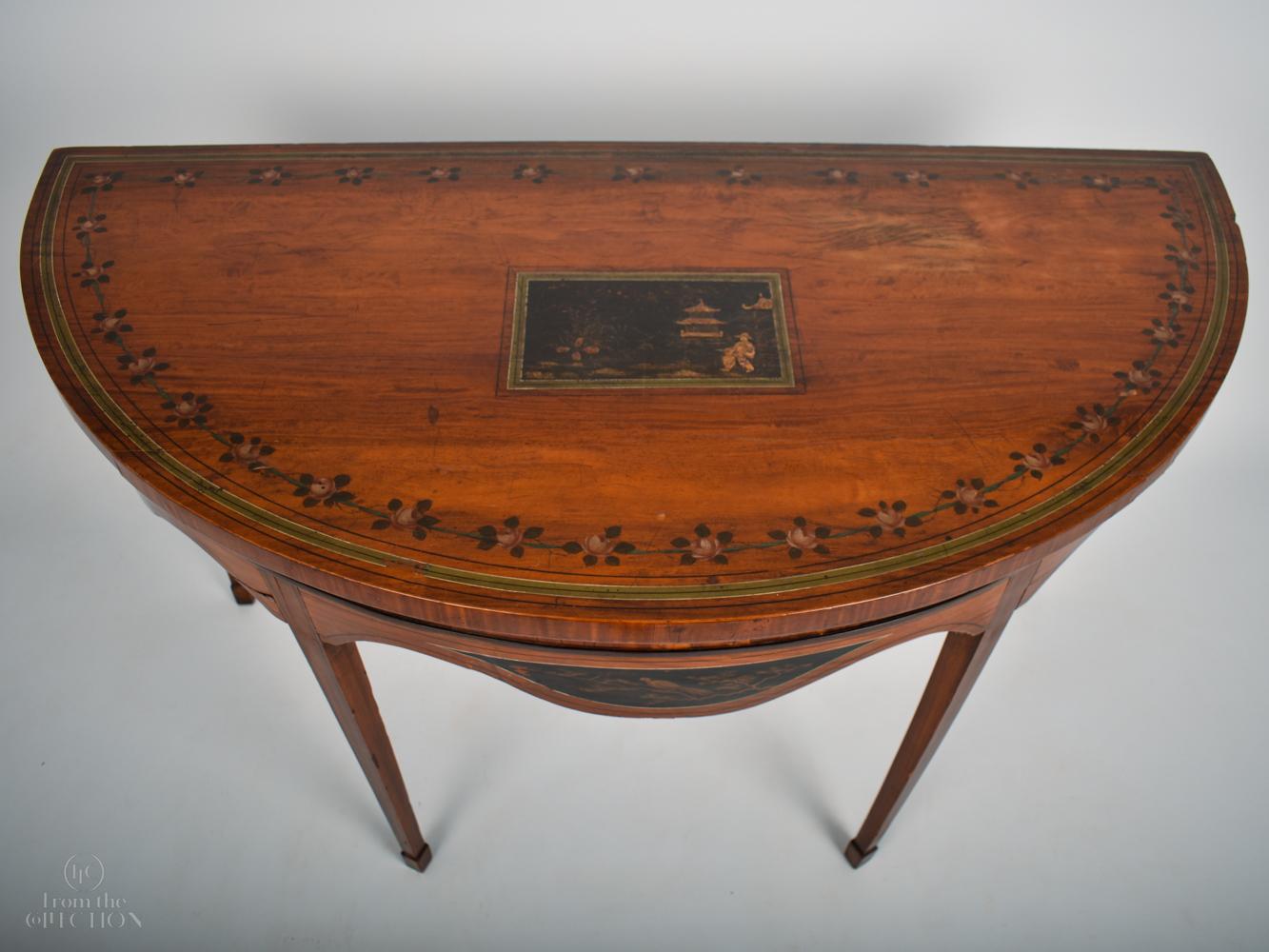 Chinese style demi-lune Pier or Console table; a rich satinwood with a dark Chinese image cartoon inlaid to the centre of the top surrounded by a garland of flowers around the border, with painted panels to the top and the front skirting and four