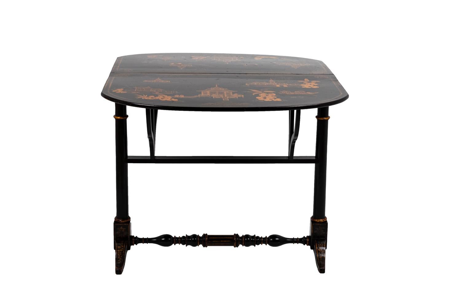 Chinese style leaf table in black lacquered wood with a gilt decor. Two leaves adorned with large cartouches framing Chinese-style landscape scenes with pagodas, junks, etc. They stand on two biped straight legs linked by a molded stud. Central