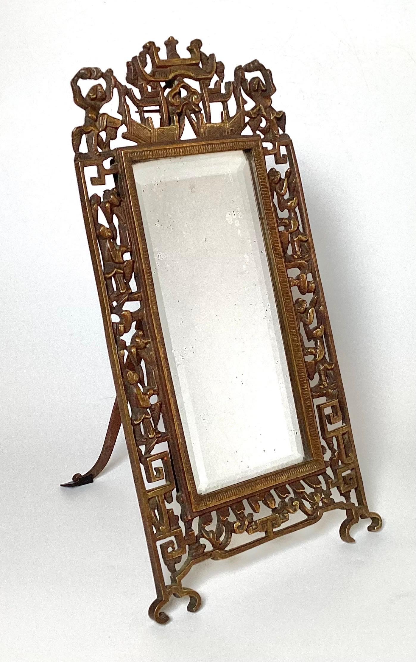 Beveled glass mirror in bronze frame.  Figures throughout frame.  Has  a wall hanging loop for wall display.  Also, has standing rod for tabletop use.