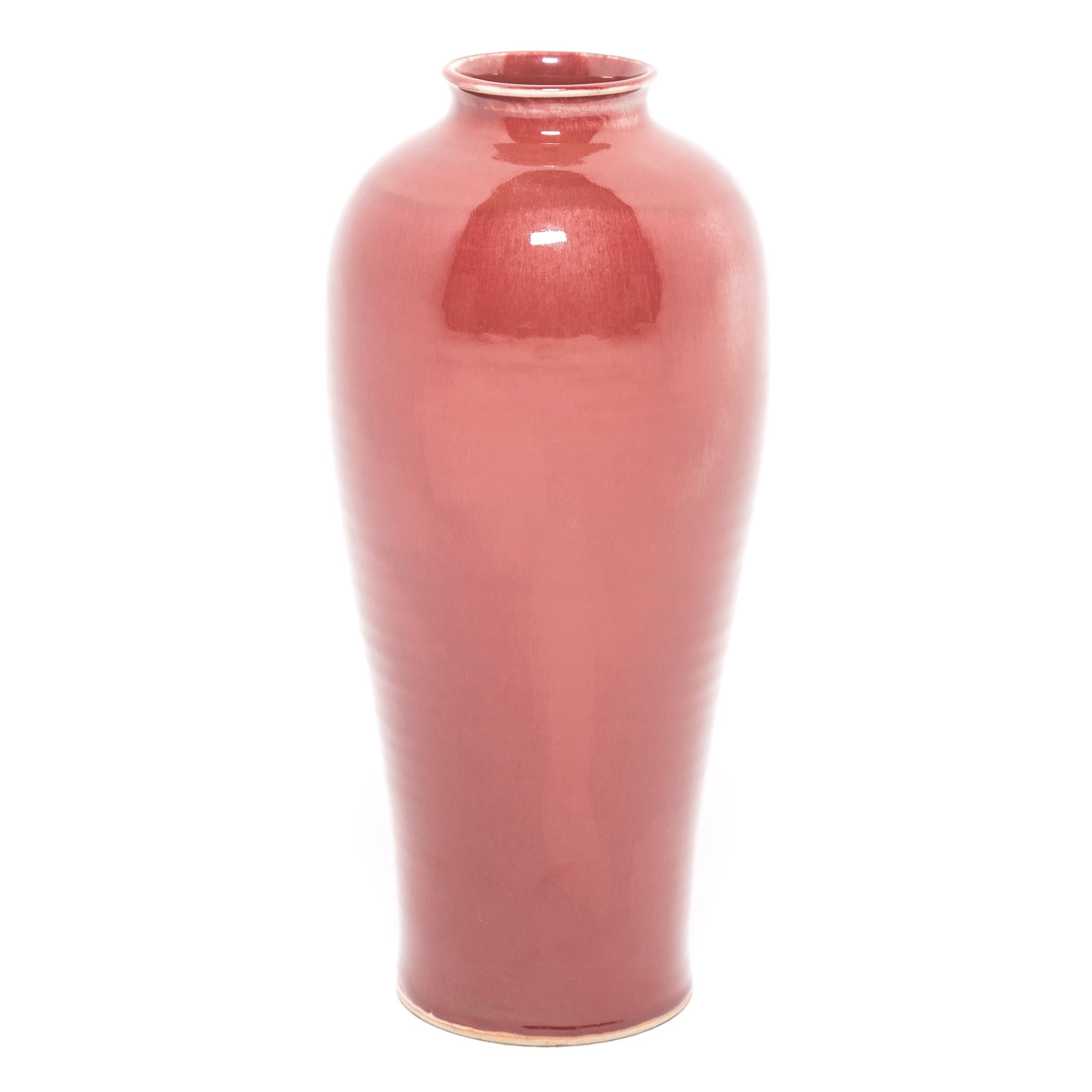 This simple yet stunning vase is sculpted in the traditional meiping vase form, historically used to hold the branches of plum trees, which are celebrated in China as symbols of strength. The tall vase's deep, rich red glaze is often called