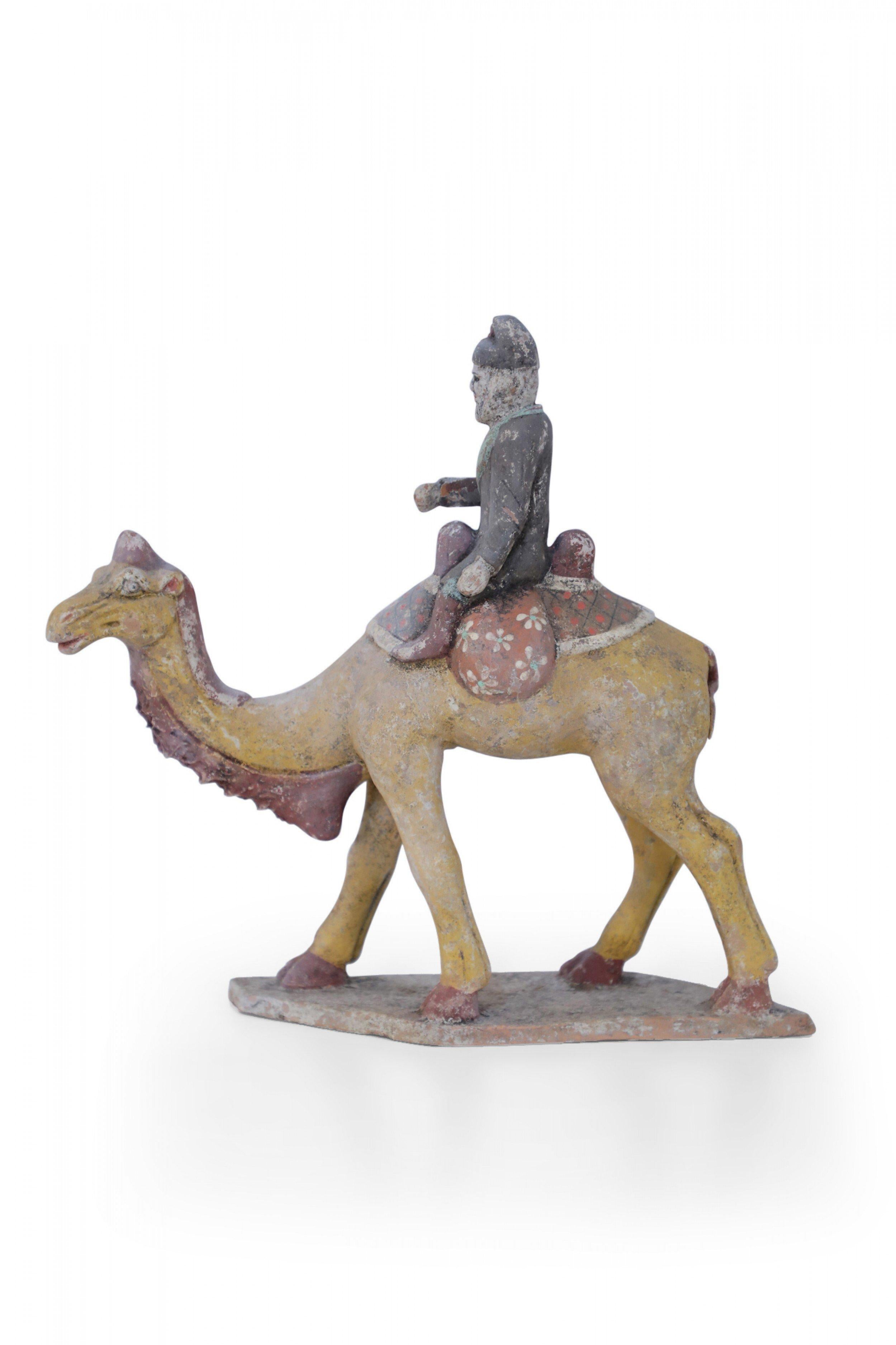 Antique Chinese Tang Dynasty-style terracotta tomb figure of a bearded rider dressed in a gray coat and brown boots riding a yellow Bactrian camel standing on a textured base.
 