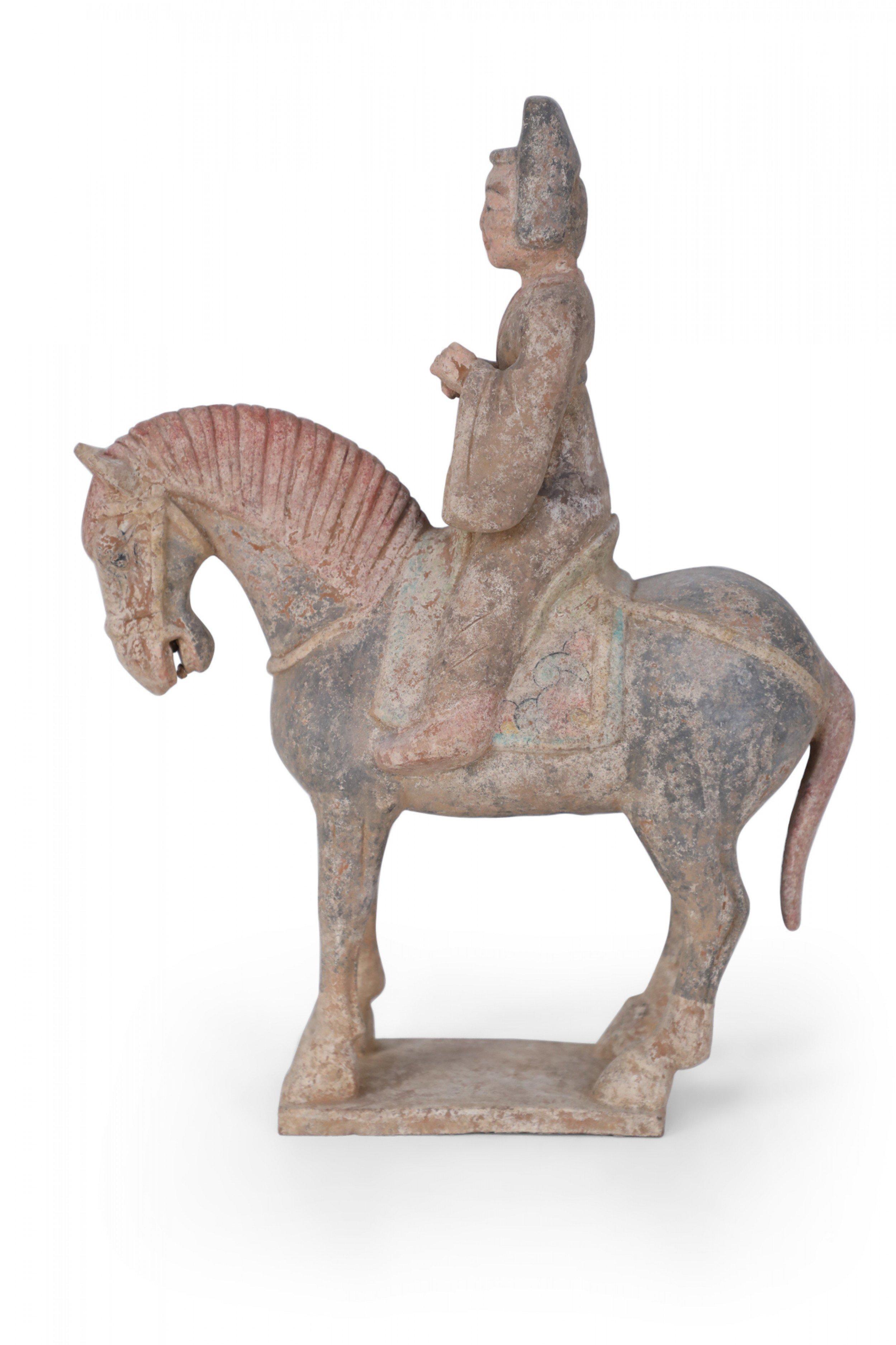 Antique Chinese Tang Dynasty-style terracotta tomb figure of a rider wearing robes sitting on a horse with a bowed head, on a square base.
      