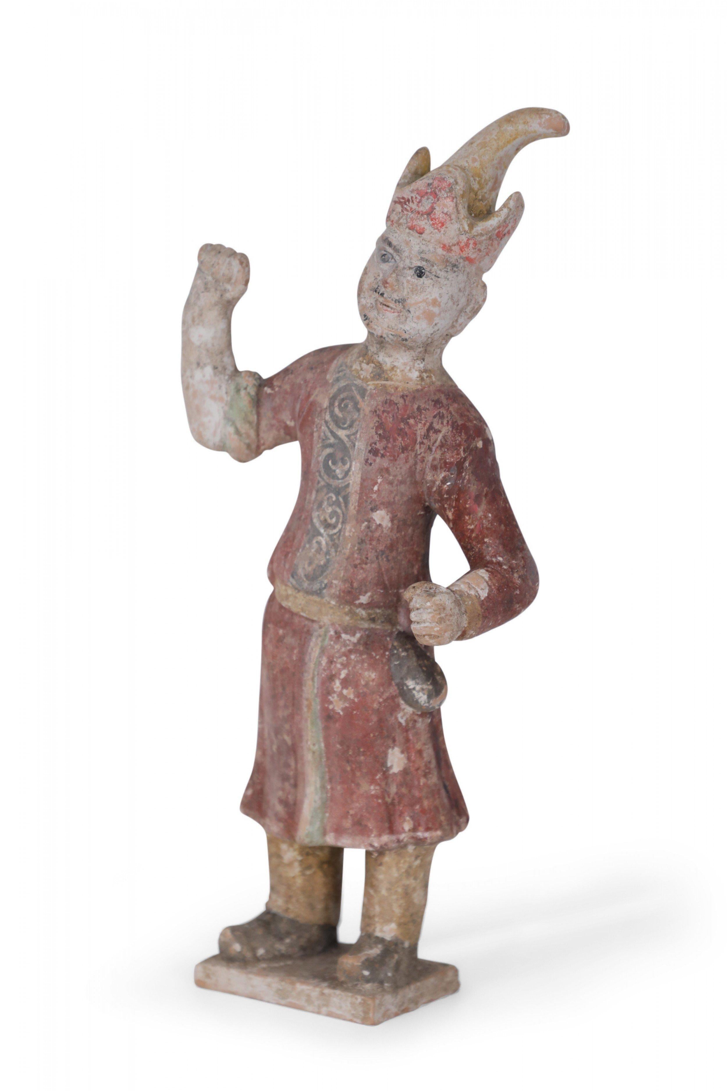 Antique Chinese Tang Dynasty-style terra cotta tomb figure of a Huren (northern tribesmen) man dressed in red robes and a prominent hat, with one fist raised in the air.
 