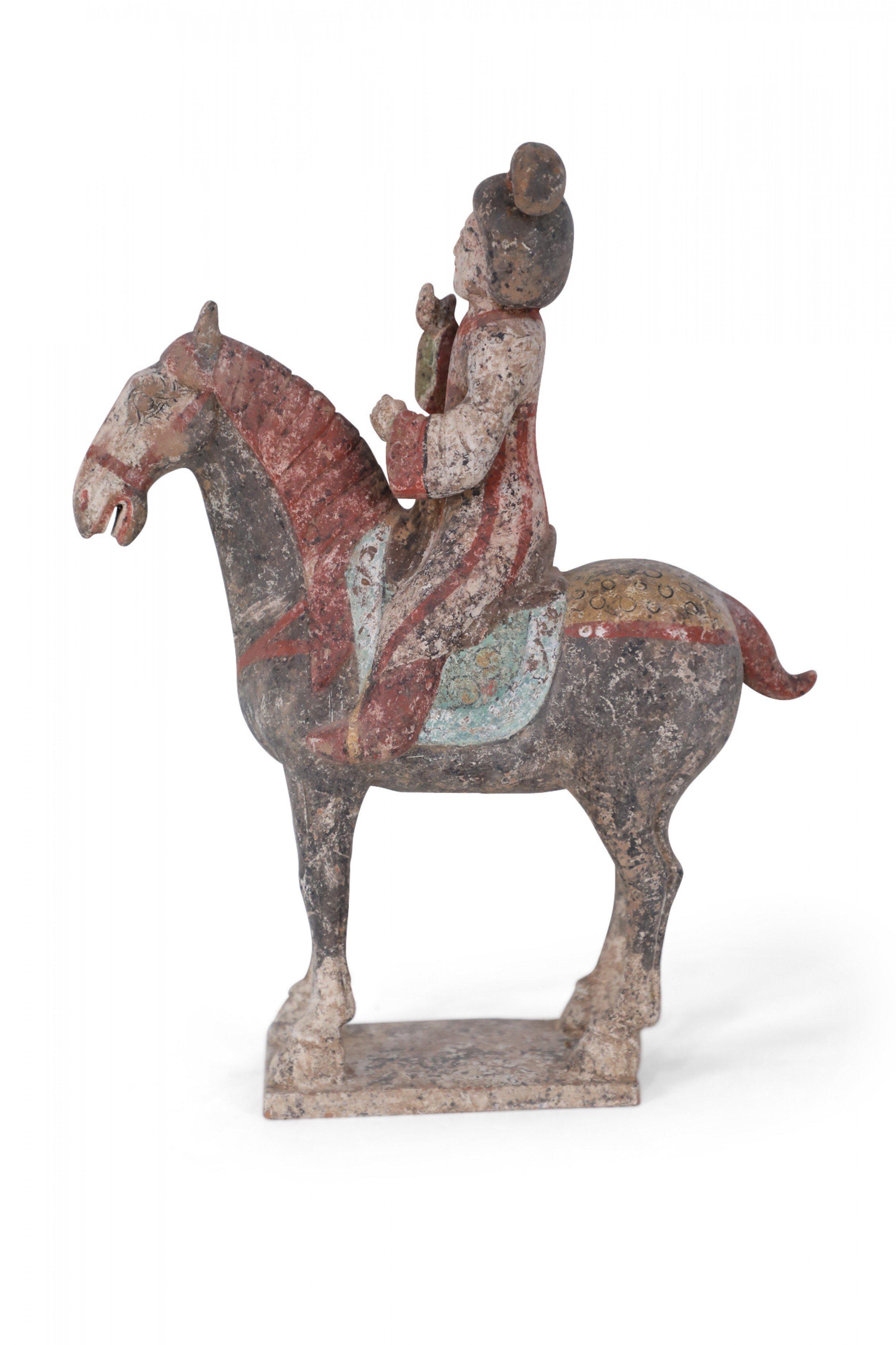 Antique Chinese Tang Dynasty-style terra cotta tomb figure of a woman dressed in gray and red robes sitting atop a blue and green saddle, on a horse that is standing on a square base.
       