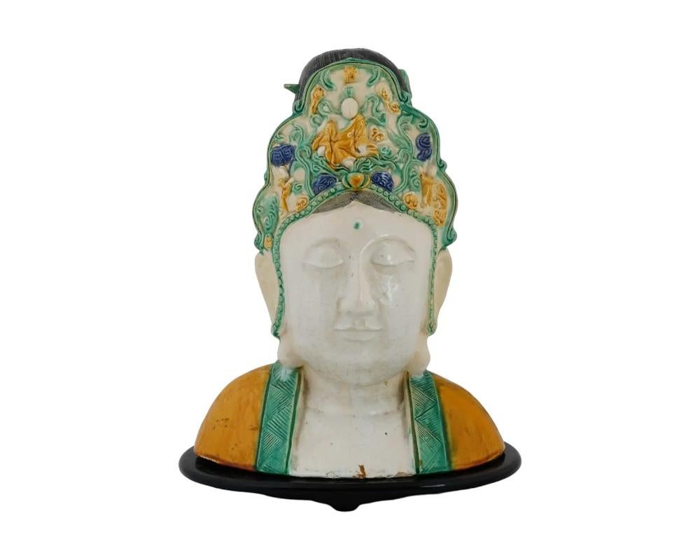 A large antique Chinese Tang dynasty manner glazed pottery bust of Guanyin with a solemn face expression and downcast eyes, wearing a headdress and robes. The bust is covered with polychrome enamel. The hair is covered with dark enamel, and the