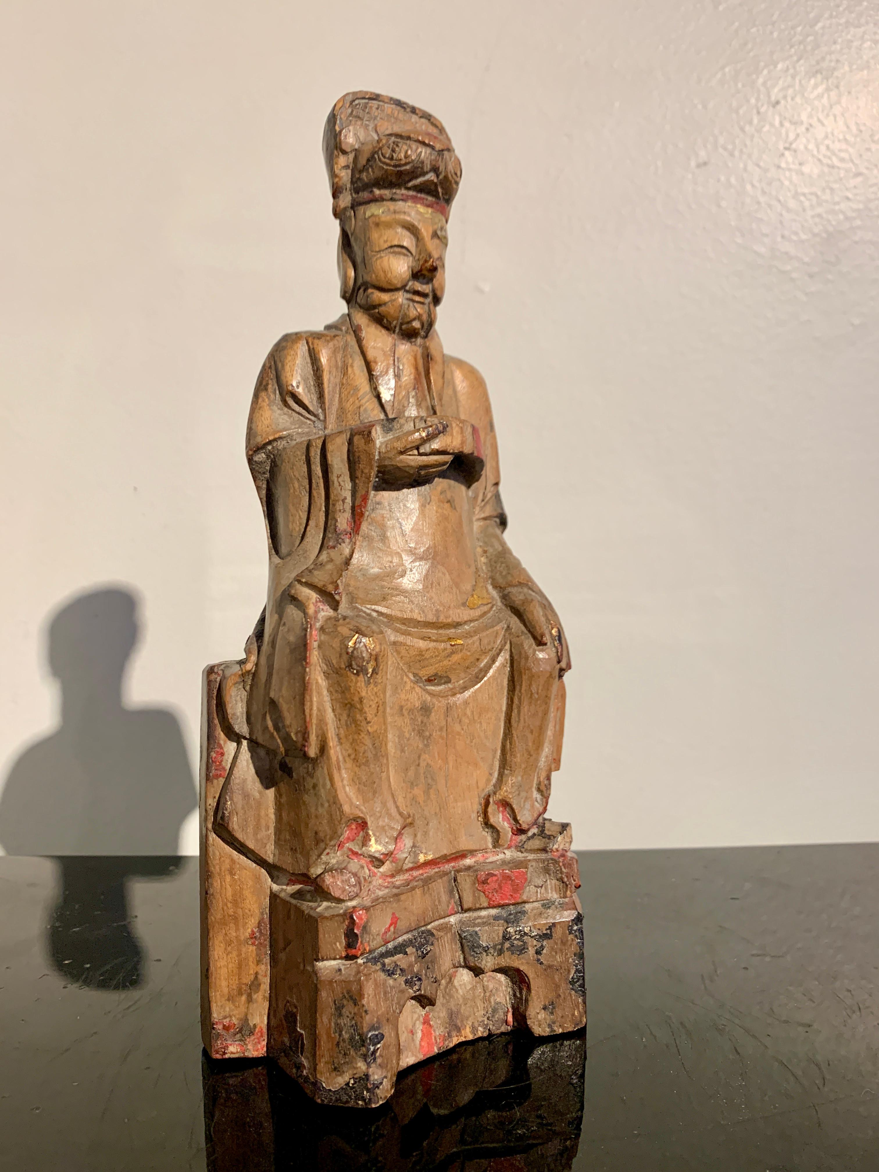 Eine charmante chinesische geschnitzte Holzfigur einer taoistischen Gottheit, möglicherweise für ein Haus oder einen persönlichen Schrein, späte Ming- oder frühe Qing-Dynastie, Mitte des 17. Jahrhunderts, Südchina. 

Die nicht identifizierte
