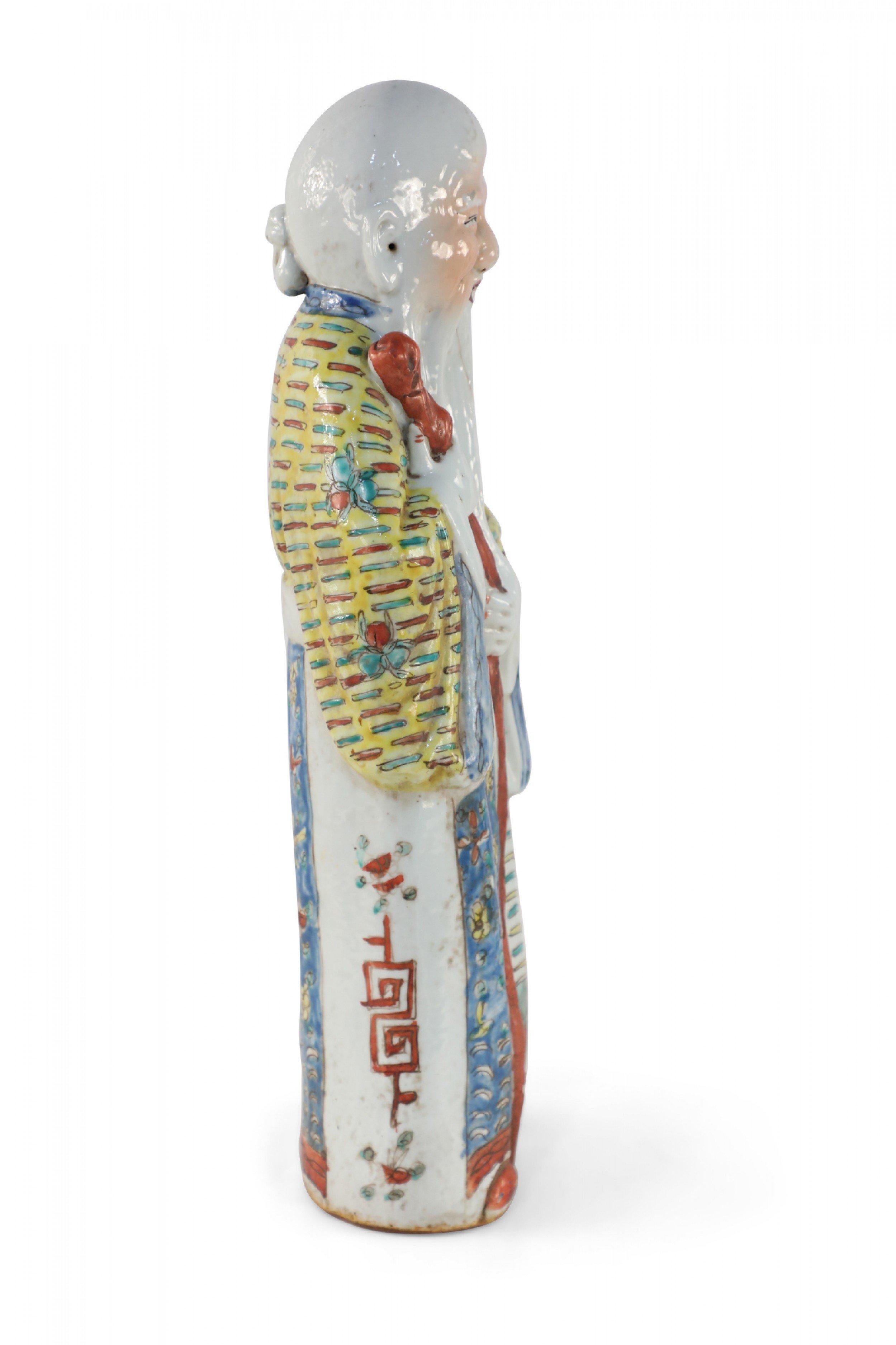 Chinese porcelain figurine with a long beard and raised forehead, clad in yellow and blue robes and holding a staff that symbolizes health and longevity in Taoist Han traditions.
  