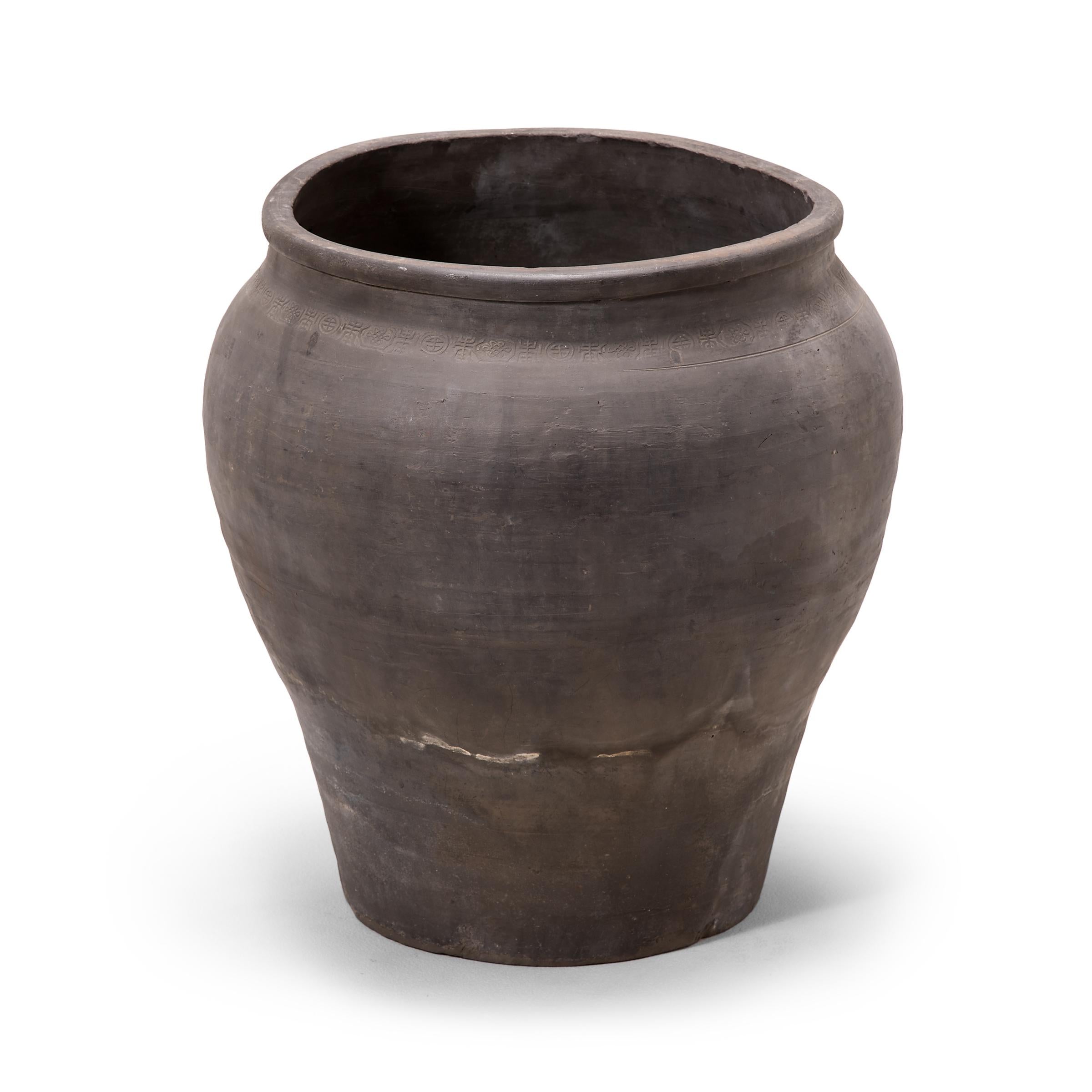 Charged with the humble task of storing dry goods, this capacious earthenware jar is distinguished by its tapered form and beautifully irregular unglazed surface. Smoke from the kiln gives the vessel its depth of color, transitioning gradually from