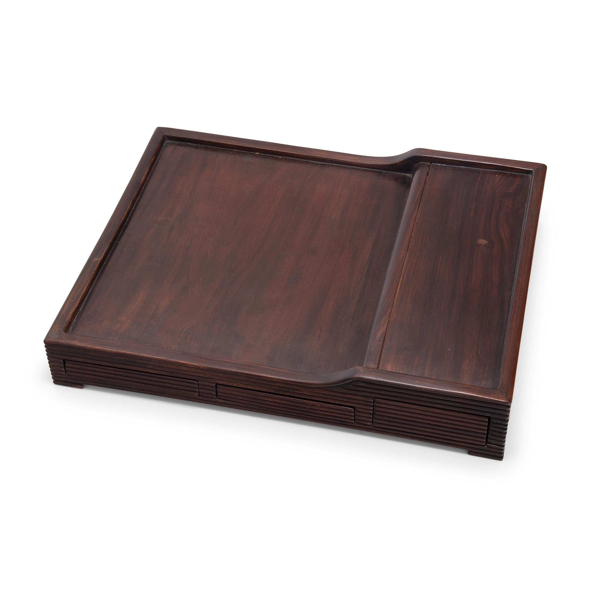Dated to the late 19th century, this elegant tea tray charms with clean lines, fine materials, and balanced proportions. Used as a surface for preparing and serving tea, the tray has a tiered top and hand-carved ridged sides concealing three shallow
