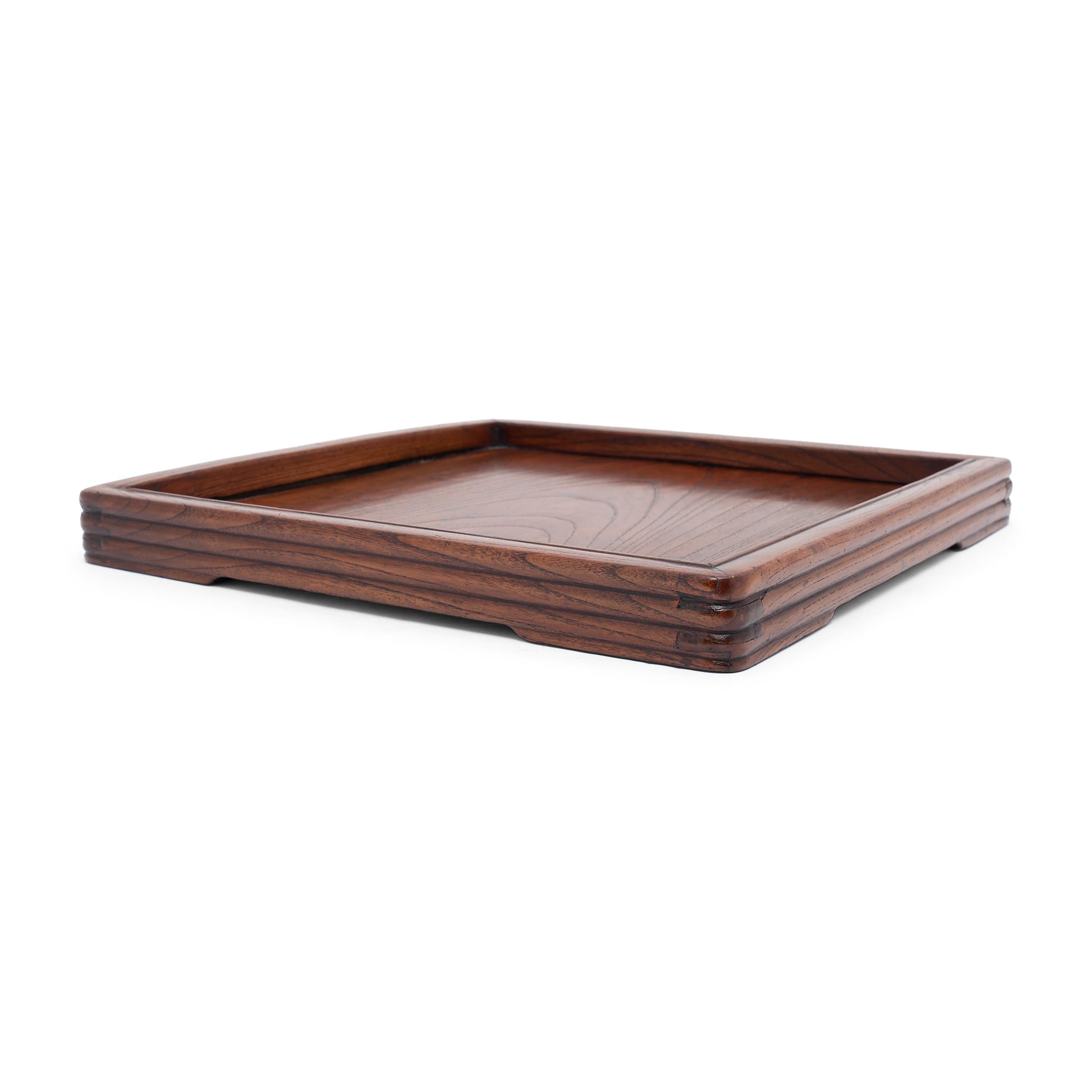 This elegant tea tray from the late 19th century owes its decorative appeal to the warm coloring and beautiful grain of northern elm (yumu). Once used to serve tea or hold scholarly implements, the shallow tray is minimally decorated, enclosed by a