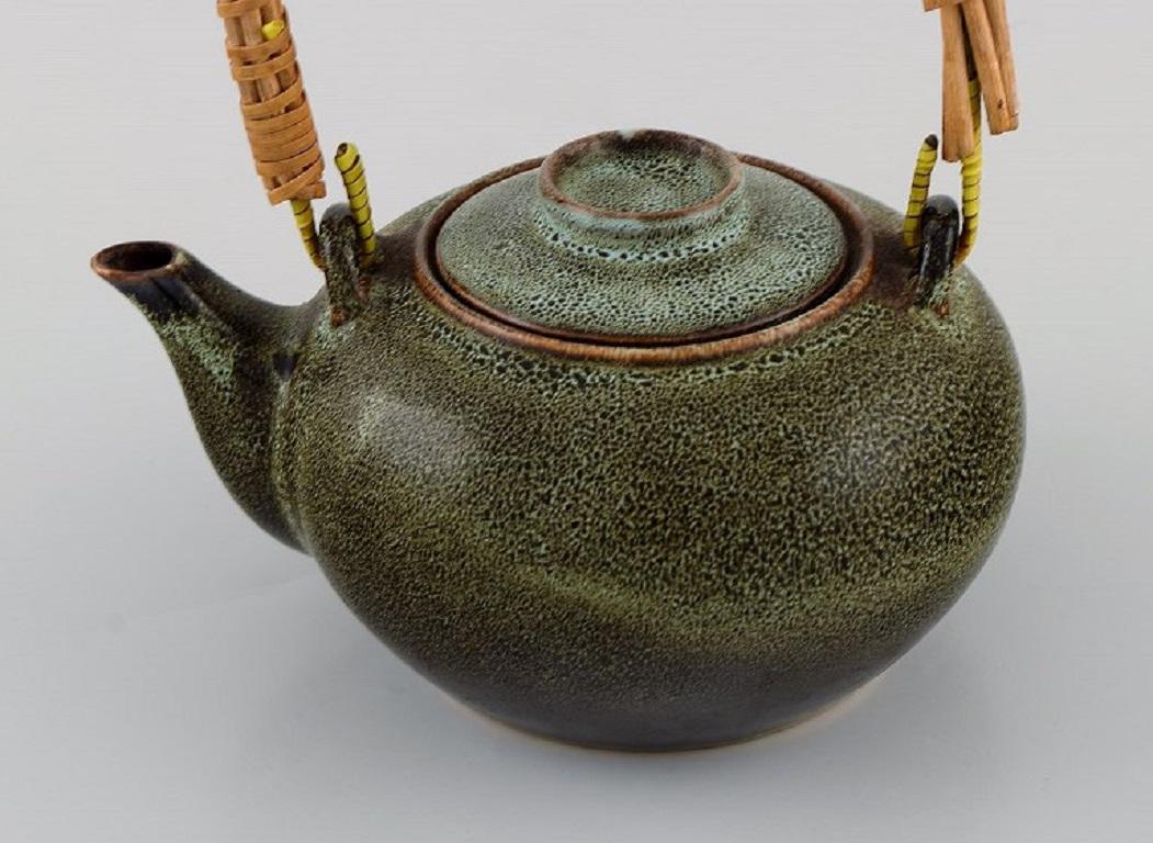 Chinesische Teekanne aus glasiertem Steingut mit Korbgeflechtgriff. 
Schöne gesprenkelte Glasur in dunkelgrünen und türkisfarbenen Farbtönen. 20. Jahrhundert.
Maße: 17,5 x 16 cm (17,5 x 16 cm) (einschließlich Griff).
In ausgezeichnetem