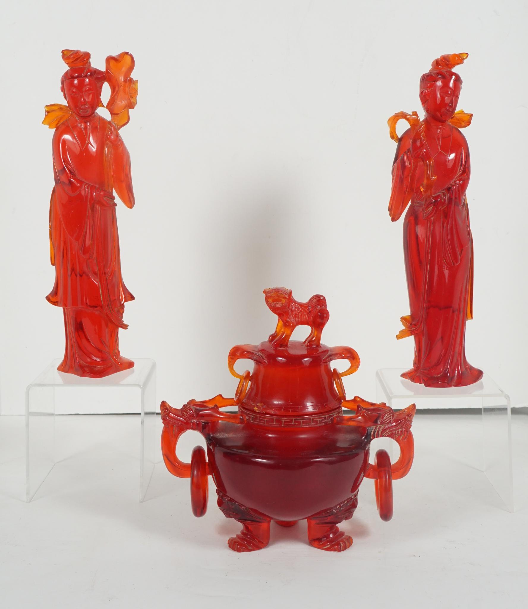 This fine colorful garniture of two different aspects of Quan Yin and accompanied by a covered censor featuring loose handles and a Buddhistic lion on the lid are made from a man-made material most often called cherry amber. Typical for the early to