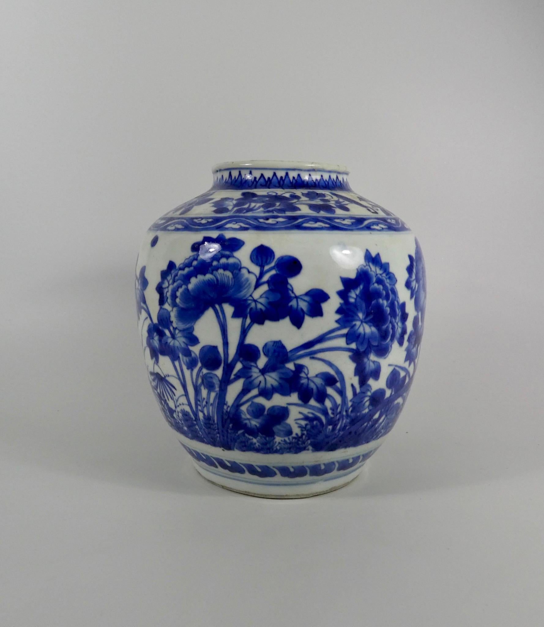 Chinese transitional porcelain jar, Shunzhi Period (1644 -1661). Well painted in underglaze blue, with a continuous scene of flowering plants, beneath a collar of stylised waves. Having a short, slightly flaring neck, painted with lappets, above a
