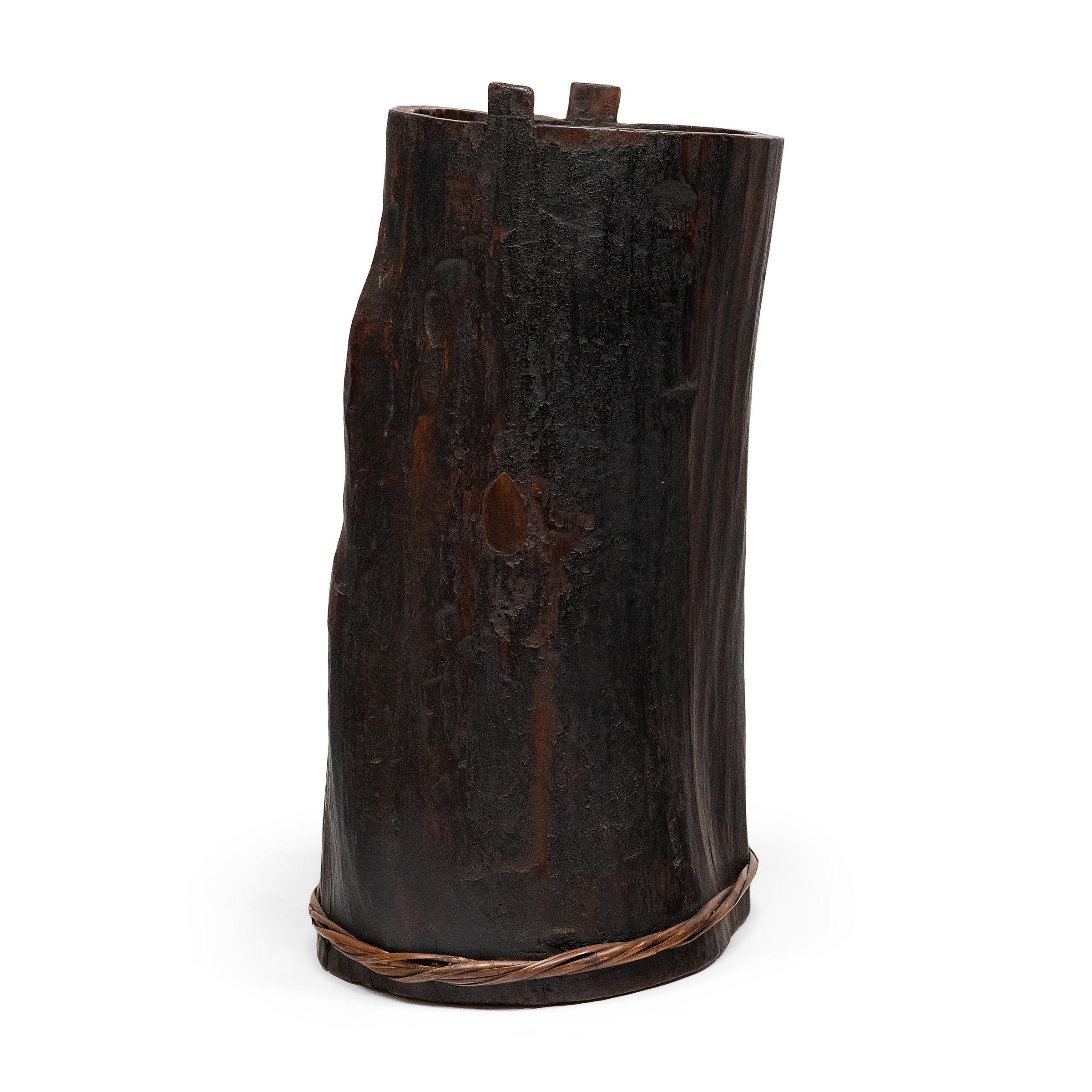 This hand-crafted wooden container dates to the mid-19th century and was likely used to store various foods or household items. Darkened by a rich patina, the container is elegantly constructed from a single block of wood with thin stripes wrapped