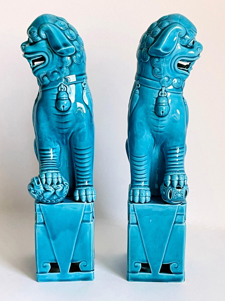 Fine and detailed pair of Chinese turquoise glazed foo dogs. The hollow biscuit porcelain figures stand raised on a rectangular base and are looking sideways with open mouths and tongues showing teeth each with a raised front paw, one resting on a