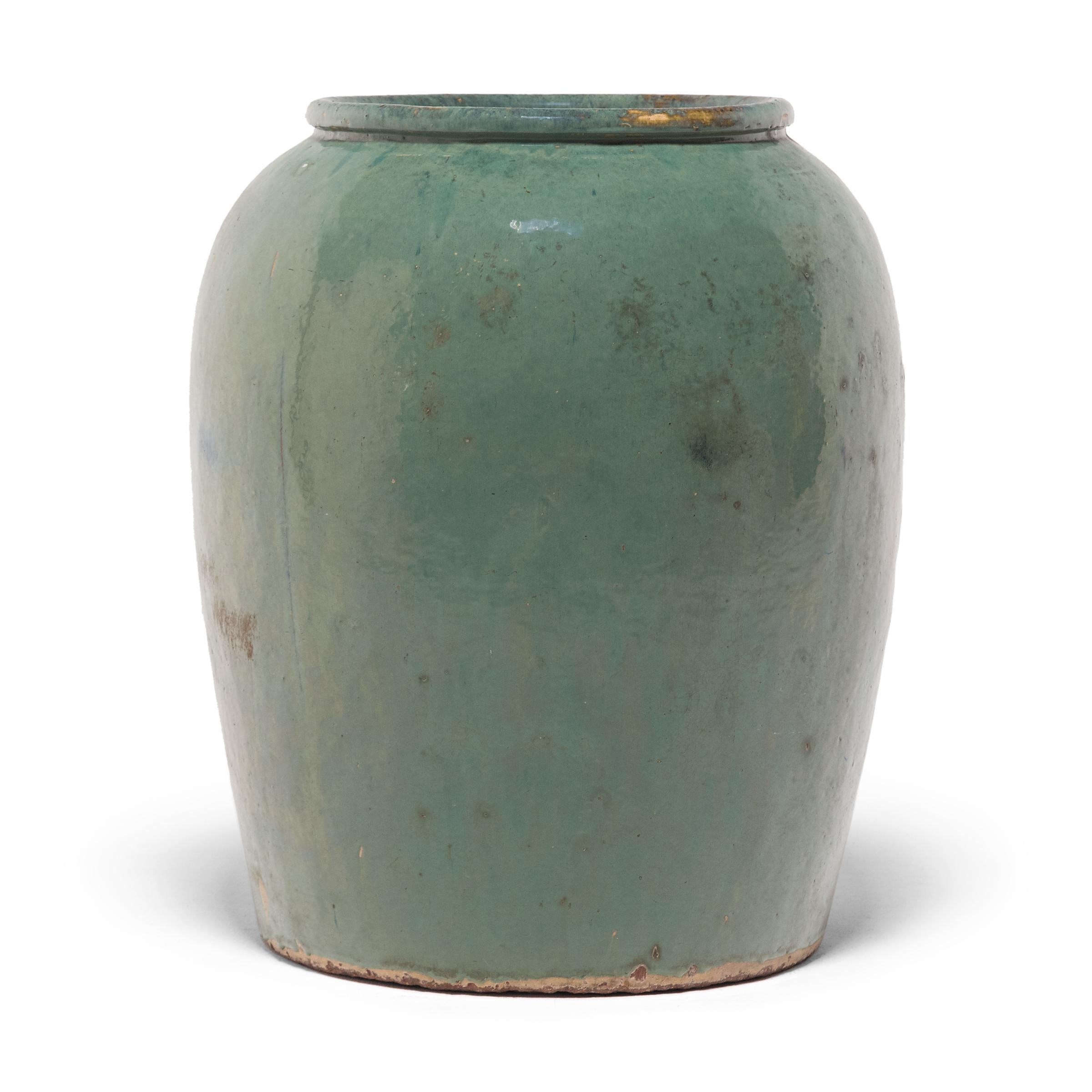 Originally used for pickling foods, this monumental early 20th-century ceramic vessel is cloaked in a beautiful celadon blue-green glaze. As the ocean colored glaze dripped down the rounded sides, lingering on each imperfection, a range of