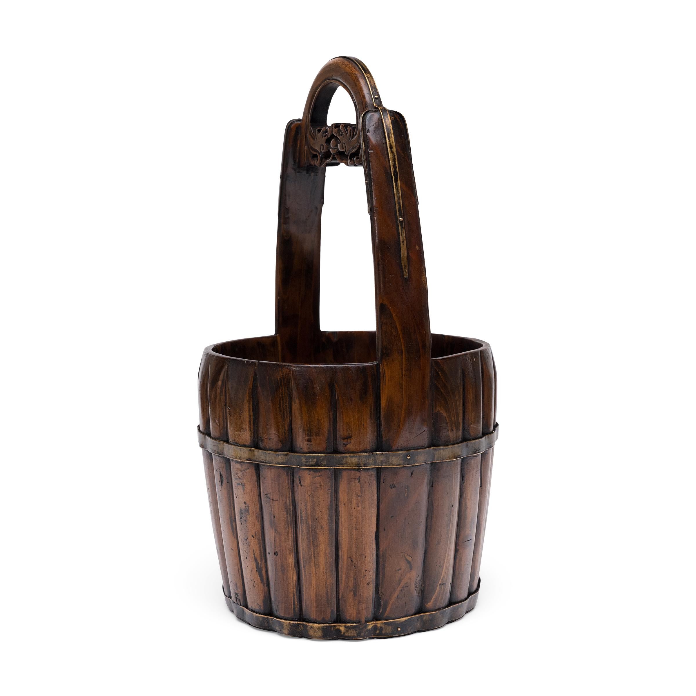 Finement ouvragé en bois d'orme et en laiton, ce joli seau en bois est un seau d'eau chinois du XIXe siècle utilisé pour puiser l'eau des puits et des jarres de pluie. Particulièrement élégant, le seau est constitué de douelles en bois reliées par
