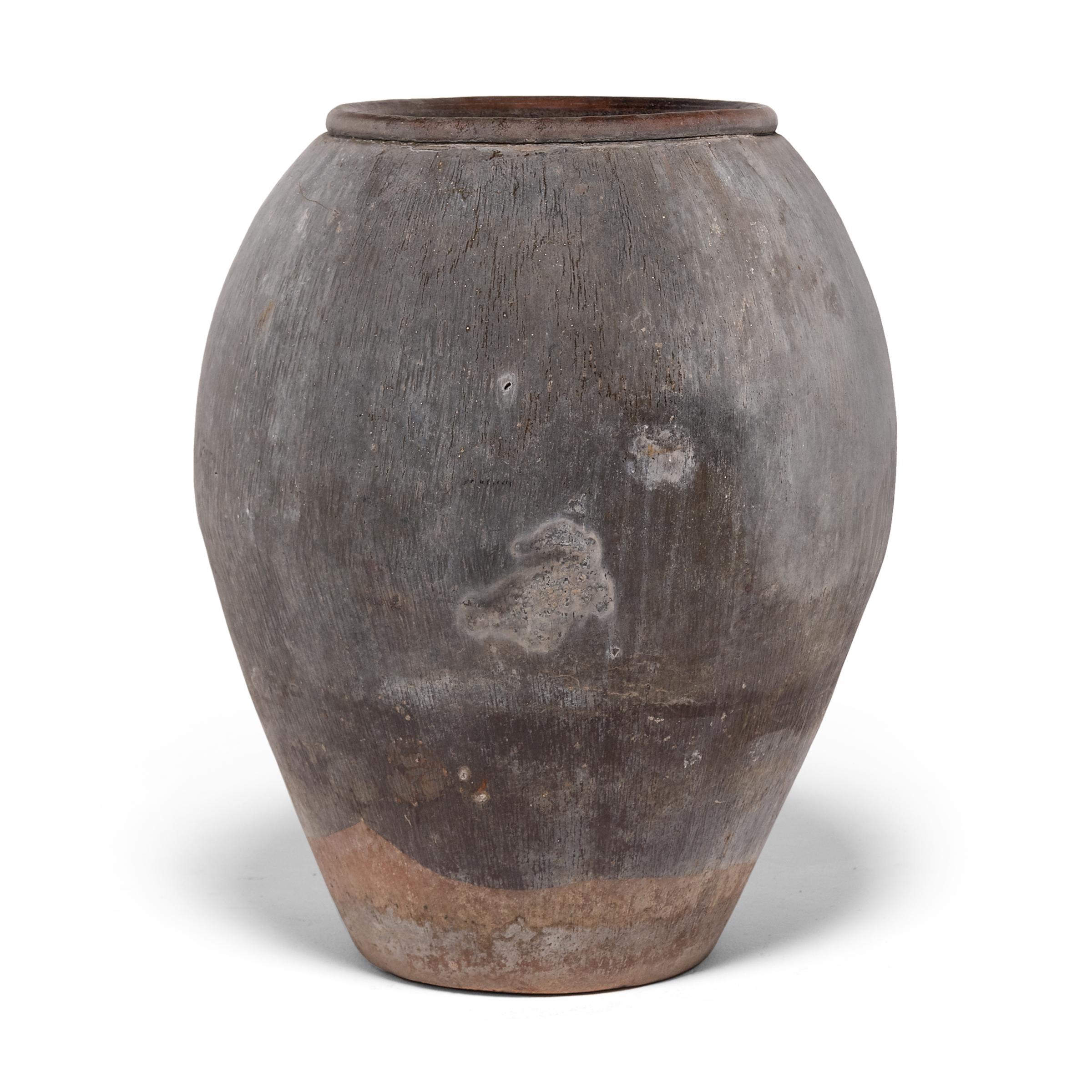 Charged with the humble task of storing dry goods, this tall earthenware jar has a graceful, tapered form and beautifully irregular unglazed surface. Contact with smoke during firing has given the vessel a gorgeous finish of neutral colors, from