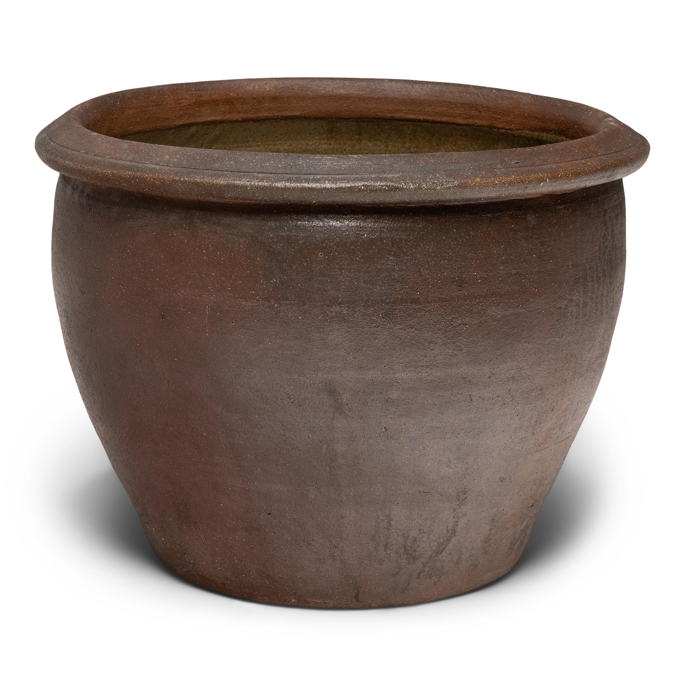 Questo laghetto basso in terracotta ha una forma minimale e una finitura splendidamente irregolare. Il vaso ha una silhouette affusolata, con una bocca larga, una base stretta e un bordo semplice e svasato. Lasciato senza decorazioni, l'esterno è