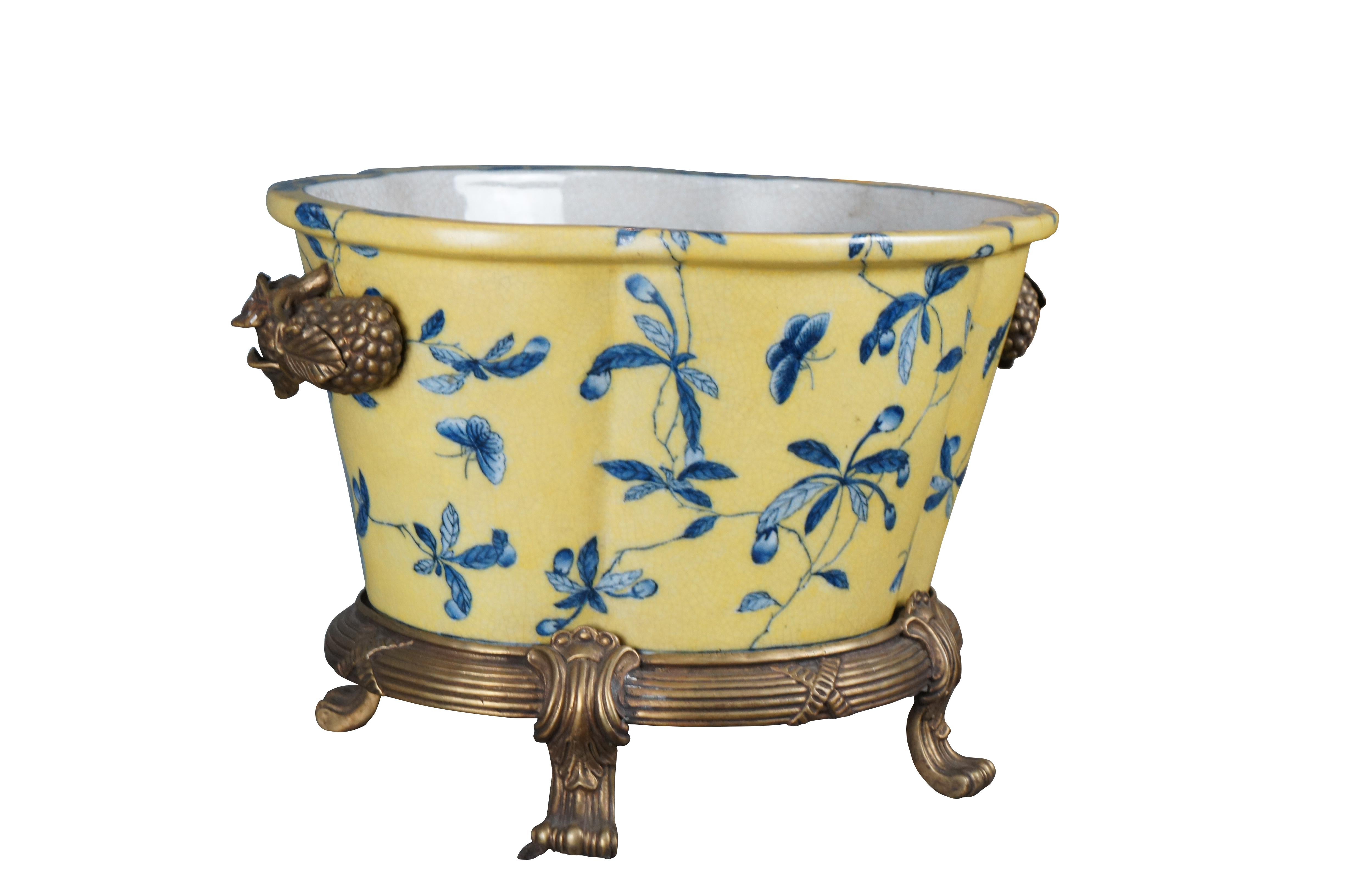 A lovely 20th Century Chinoiserie cachepot by United Wilson (JUWC). Features a lobed porcelain body in yellow with blueberry shrub and butterfly motif. The planter rests on a French inspired bronze base with contoured feet. Handles are high relief