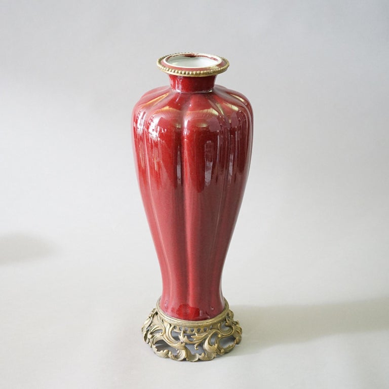A Chinese porcelain vase offers porcelain construction in vermillion red glaze with foliate cast bronze mounts, 20th century

Measures- 20.75''H x 7.75''W x 7.75''D.