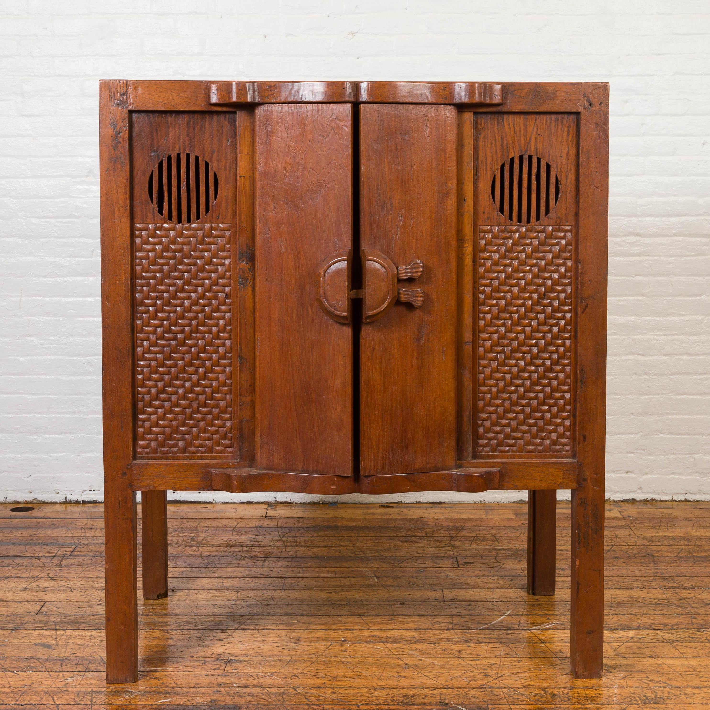 A vintage Chinese wooden cabinet on legs from the mid-20th century, with two doors and carved panels. Showcasing a linear Silhouette and a brown patina, this Chinese cabinet features two narrow doors in the center of its façade, closing thanks to a