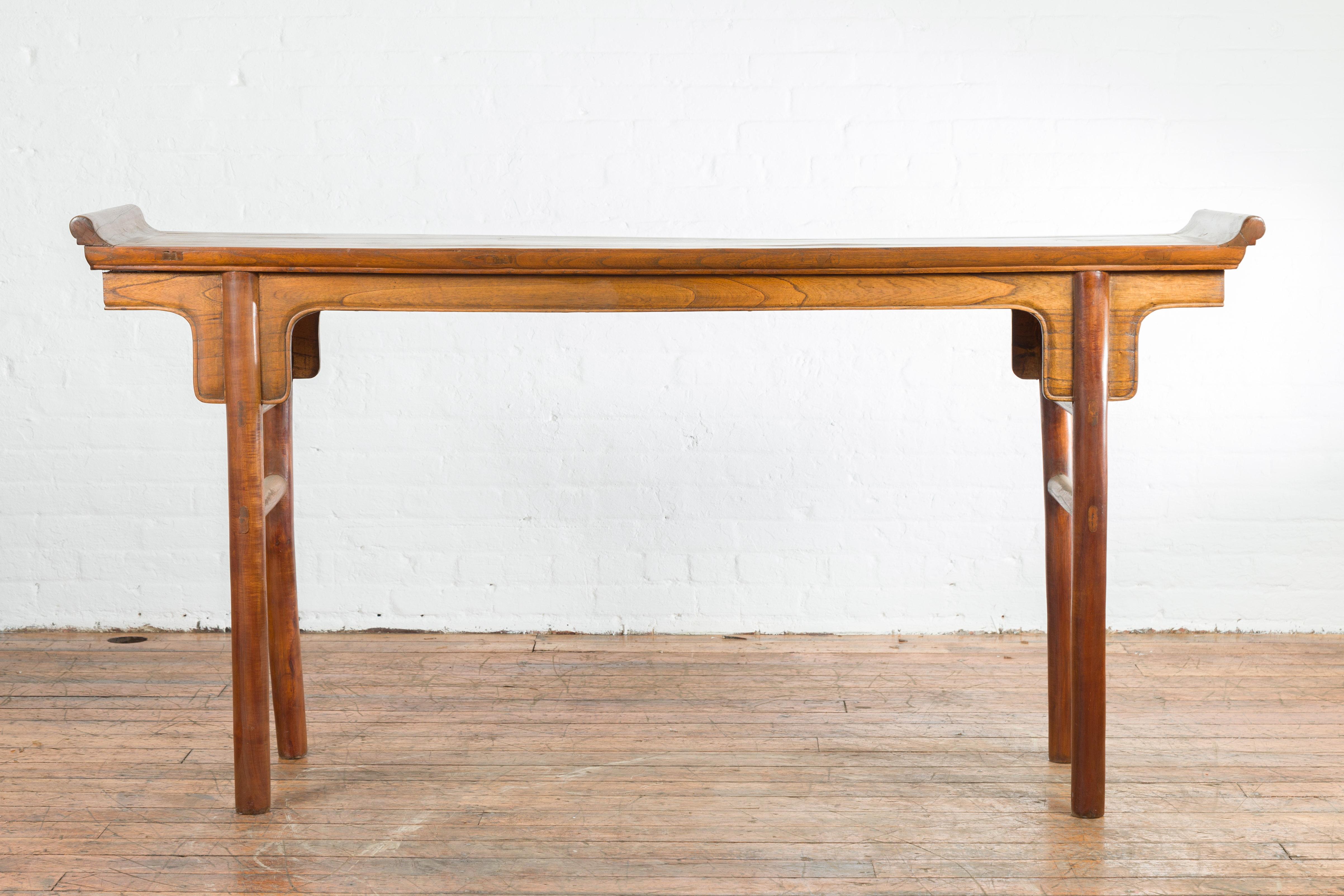 A Chinese vintage altar console table from the mid 20th century, with everted flanges and natural brown patina. Created in China during the midcentury period, this altar console table features a narrow rectangular top flanked with everted flanges,