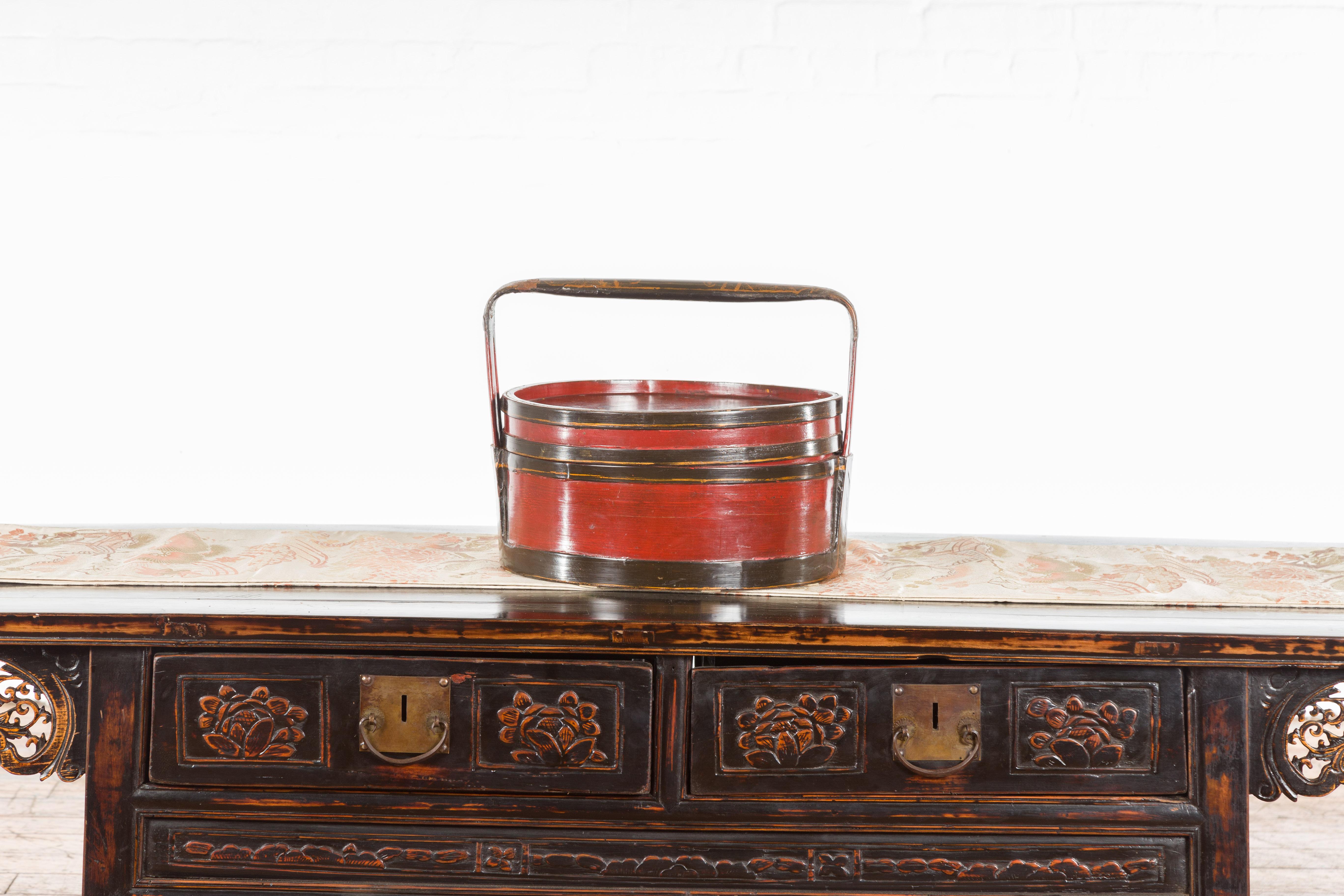 A Chinese vintage black and red lacquer picnic basket from the mid 20th century, with gilt Chinoiserie décor. Created in China during the midcentury period, this red and black lacquer picnic basket draws our attention with its circular lid adorned