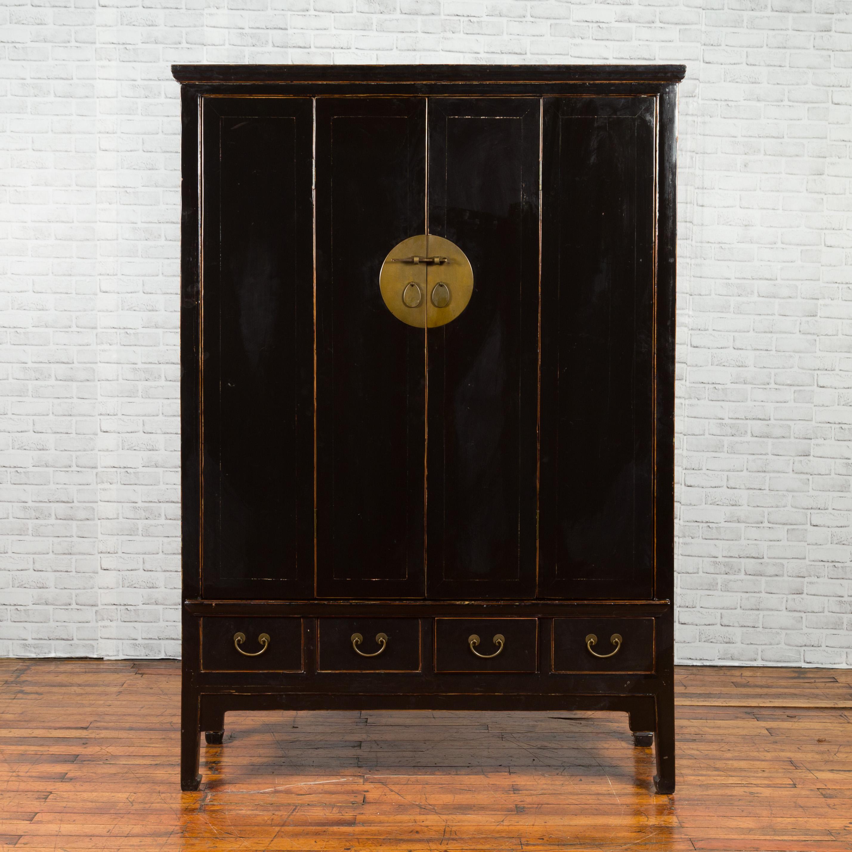 A Chinese vintage black lacquer bi-fold accordion door cabinet from the mid-20th century, with brass medallion and drawers. Created in China during the mid-century period, this tall cabinet features a black lacquered structure perfectly contrasting