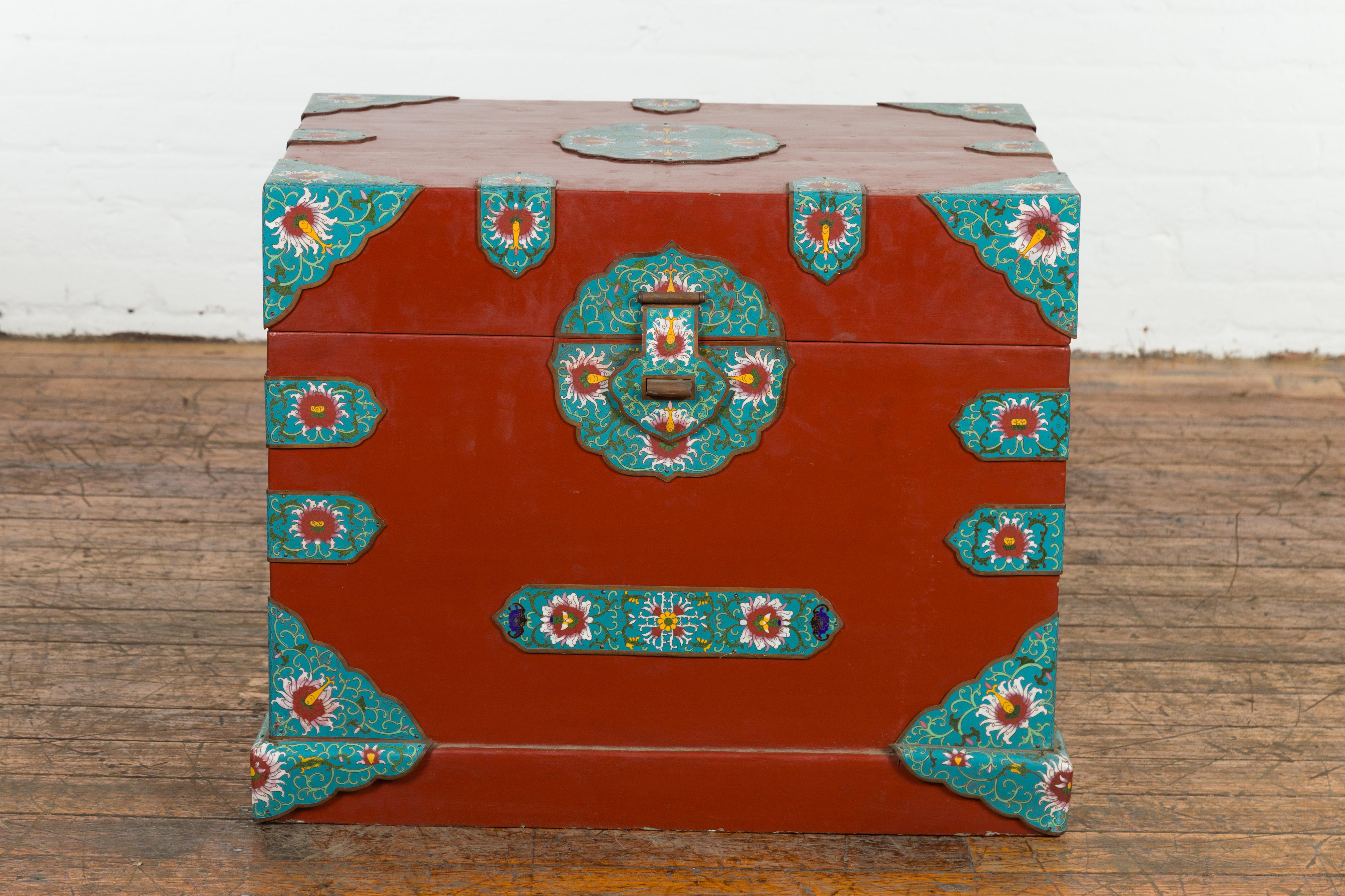 A vintage Chinese blanket chest from the mid 20th century with red lacquer ground, cloisonné décor and lateral handles. Created in China during the midcentury period, this blanket chest features a rectangular lid adorned with an ornate cloisonné