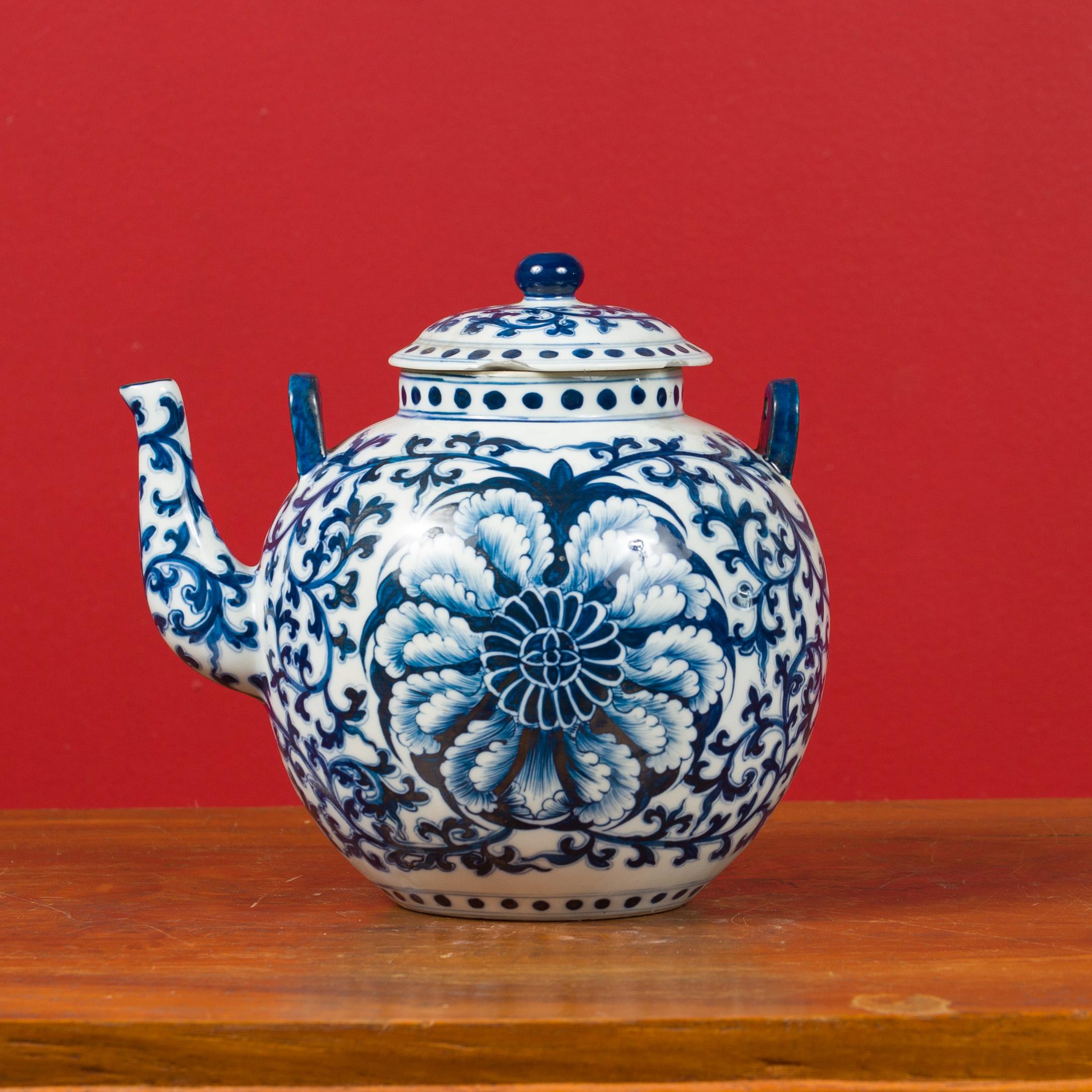 A Chinese vintage blue and white porcelain teapot from the mid 20th century. Created in China during the midcentury period, this lovely teapot features a circular lid with petite sphere at the top, sitting above a round body adorned with an abundant