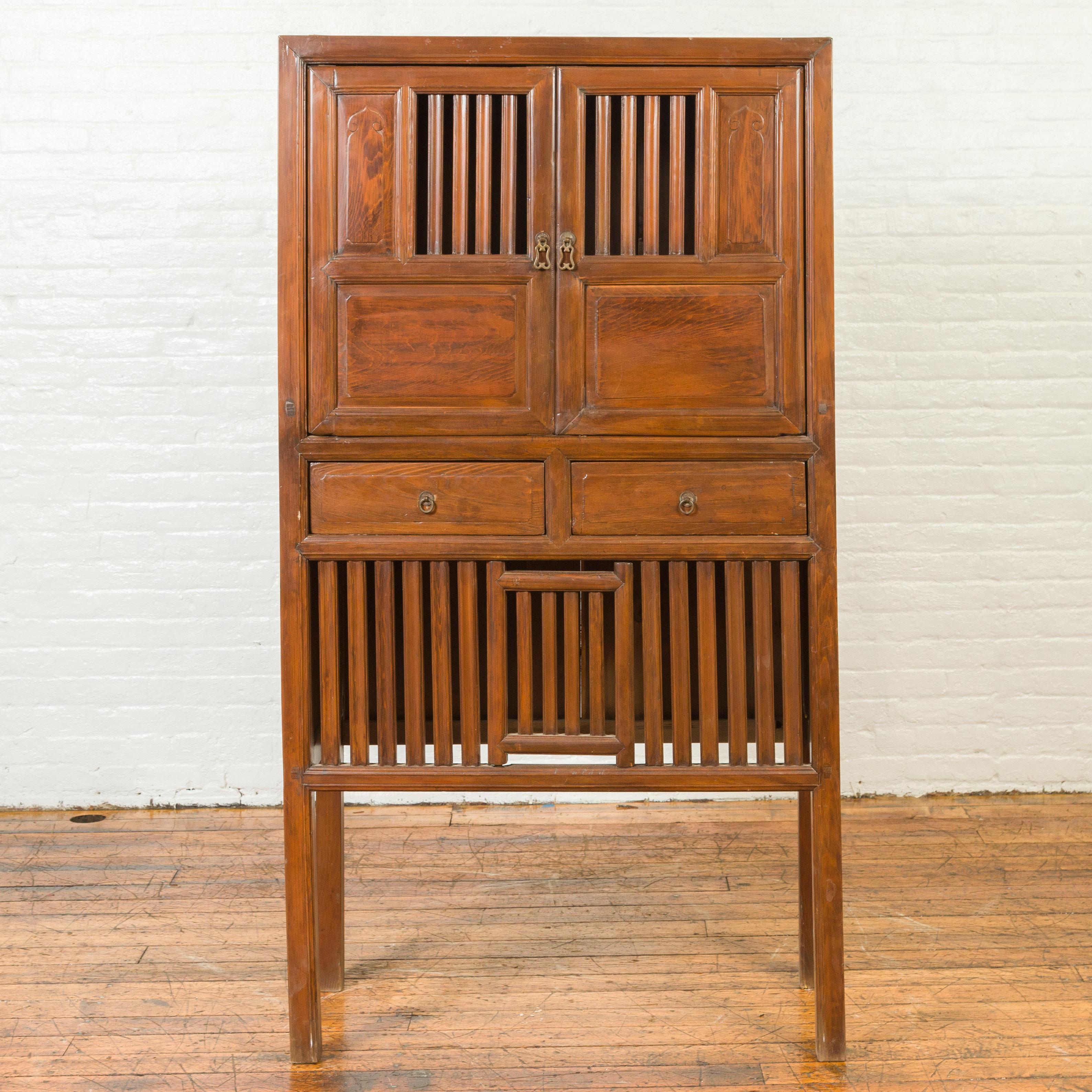 A Chinese vintage cabinet from the mid-20th century, with fretwork design, doors, drawers and tall legs. Created in China during the midcentury period, this wooden cabinet features a linear silhouette accented by perfectly organized fretwork