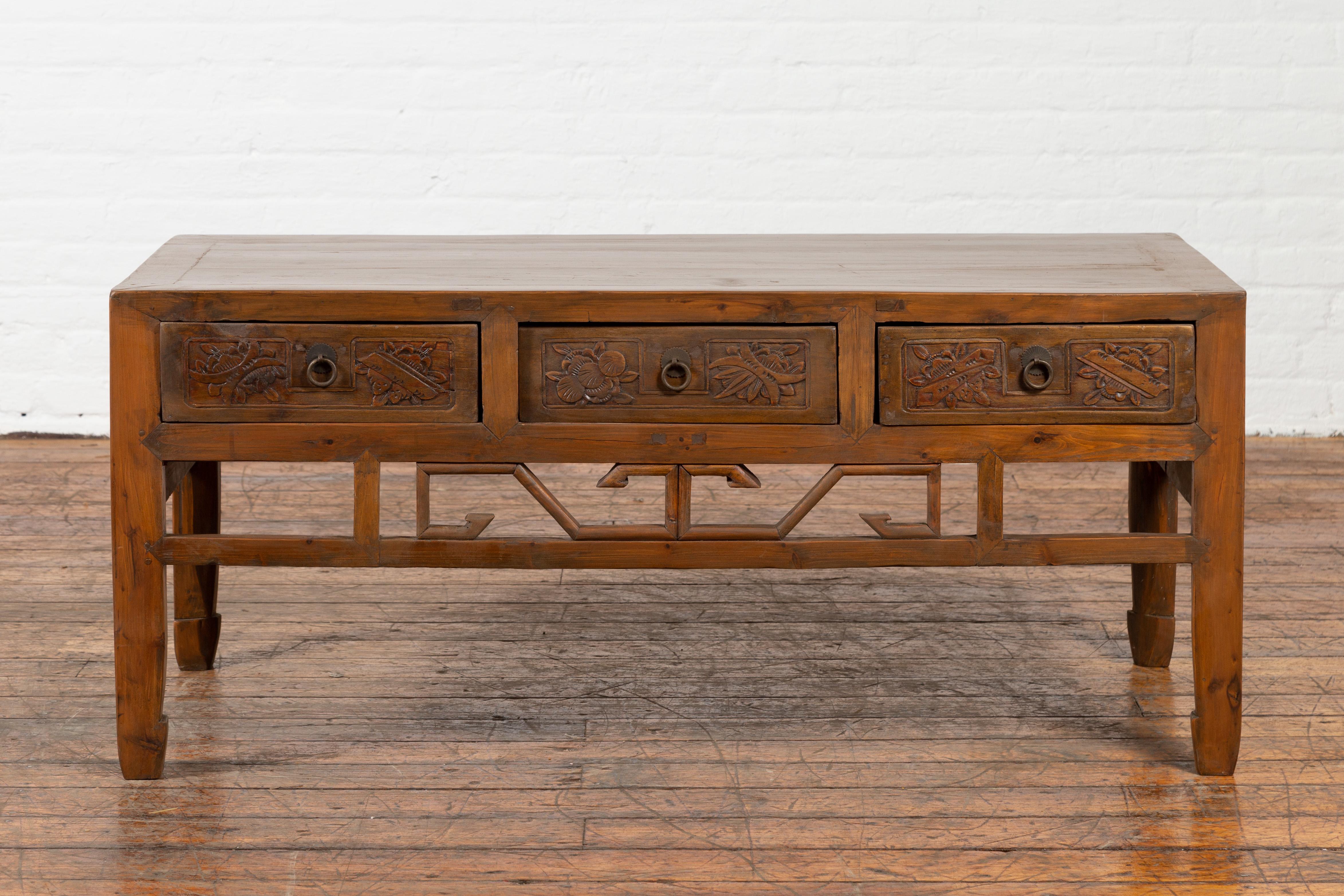 A Chinese vintage coffee table from the mid 20th century, with three carved drawers, pierced apron and horse hoof feet. Created in China during the midcentury period, this vintage coffee table features a rectangular planked top sitting above three