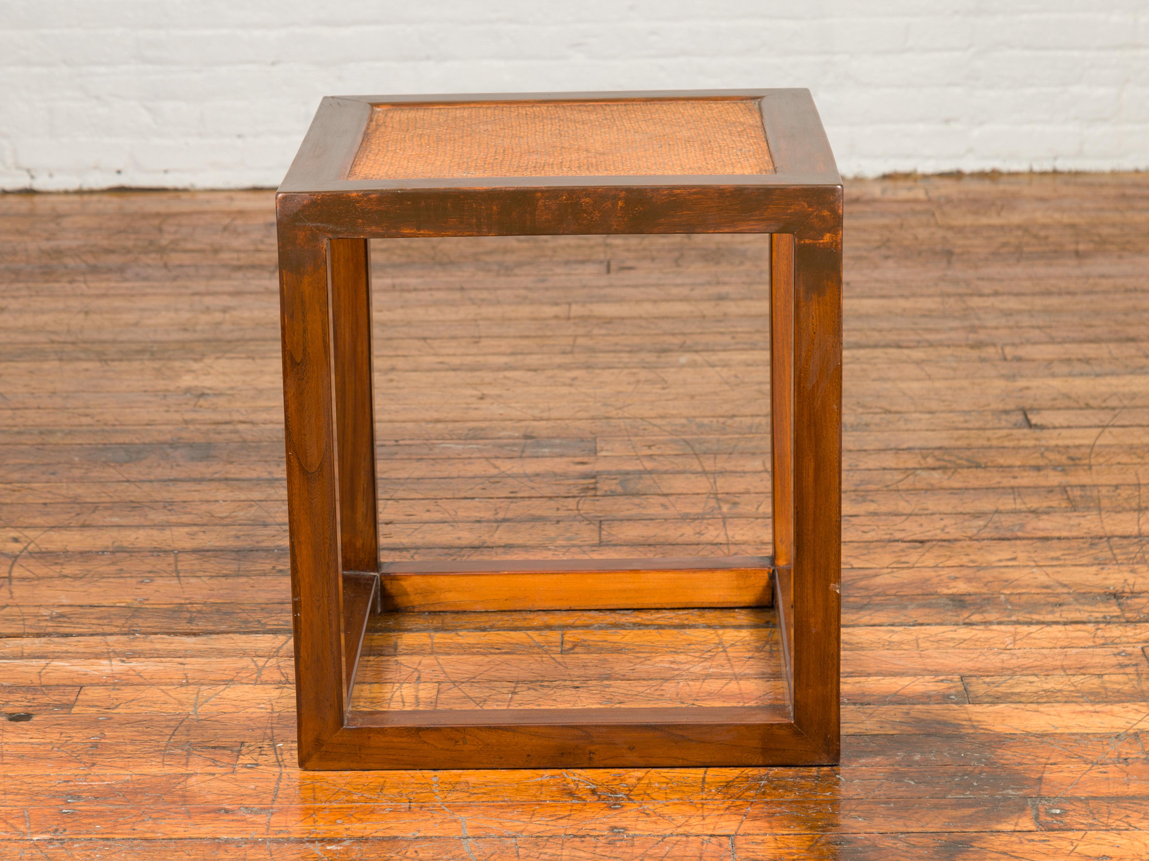 A minimalist cubic side table from the mid-20th century, with rattan top and straight legs. Immerse yourself in the sleek and simplistic elegance of this minimalist cubic side table from the mid-20th century. This piece, embodying the midcentury