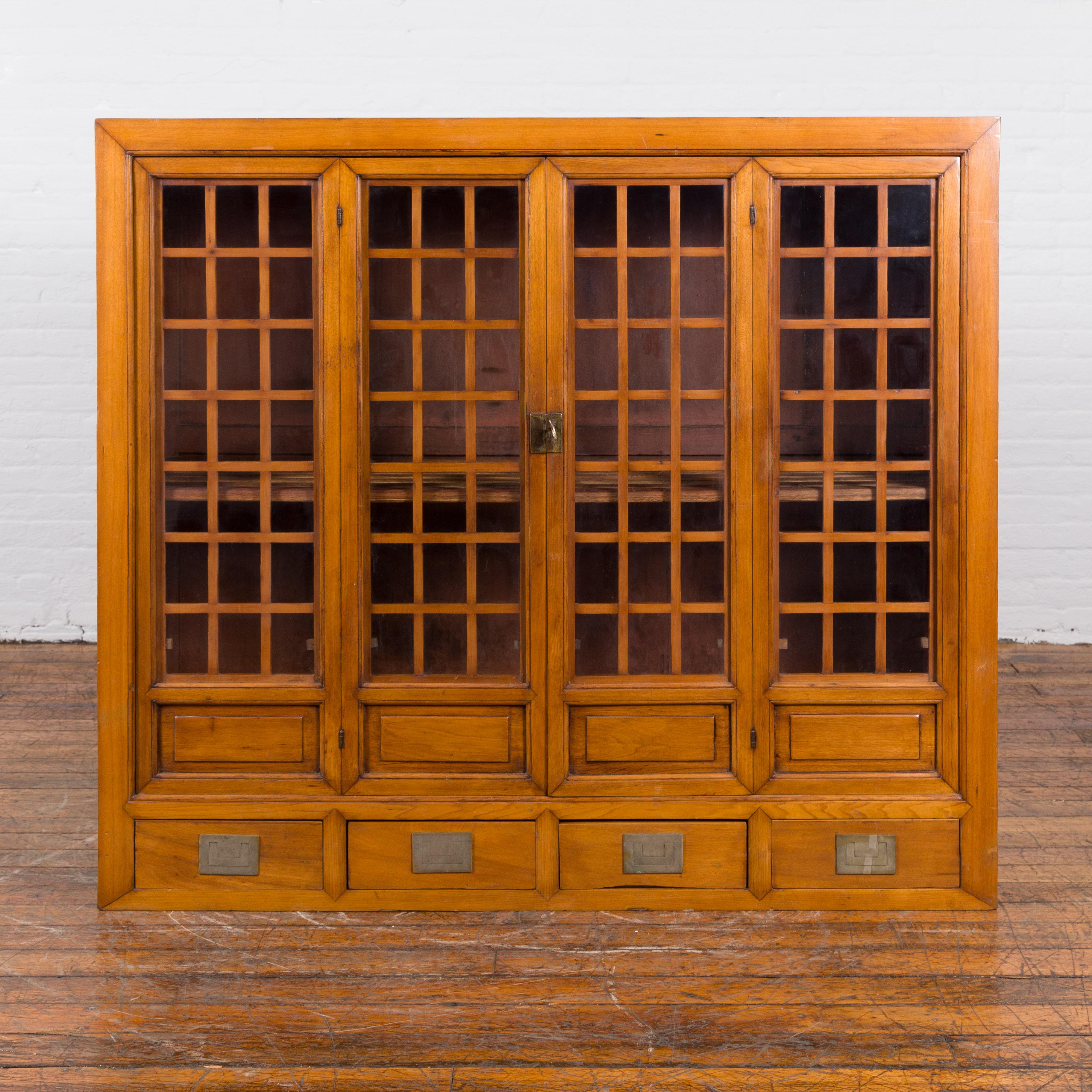A Chinese vintage display cabinet from the mid 20th century, with glass doors and four drawers. Created in China during the midcentury period, this display cabinet features a linear silhouette perfectly complimented by a handsome honey brown patina.