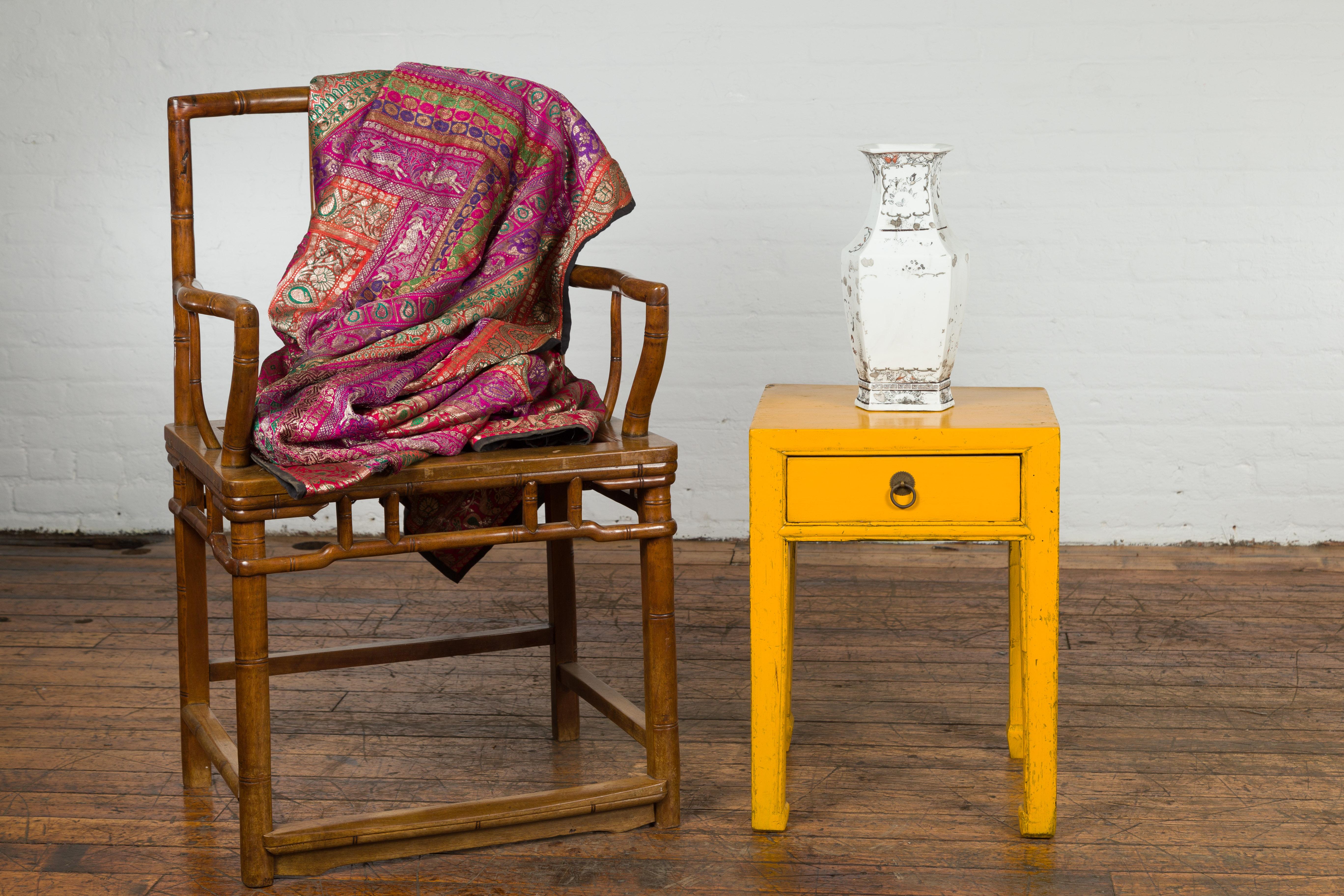 A small vintage Chinese side table from the mid 20th century, with yellow lacquer, distressed patina, single drawer, and horse hoof legs. Created in China during the mid century period, this small side table attracts our attention with its petite