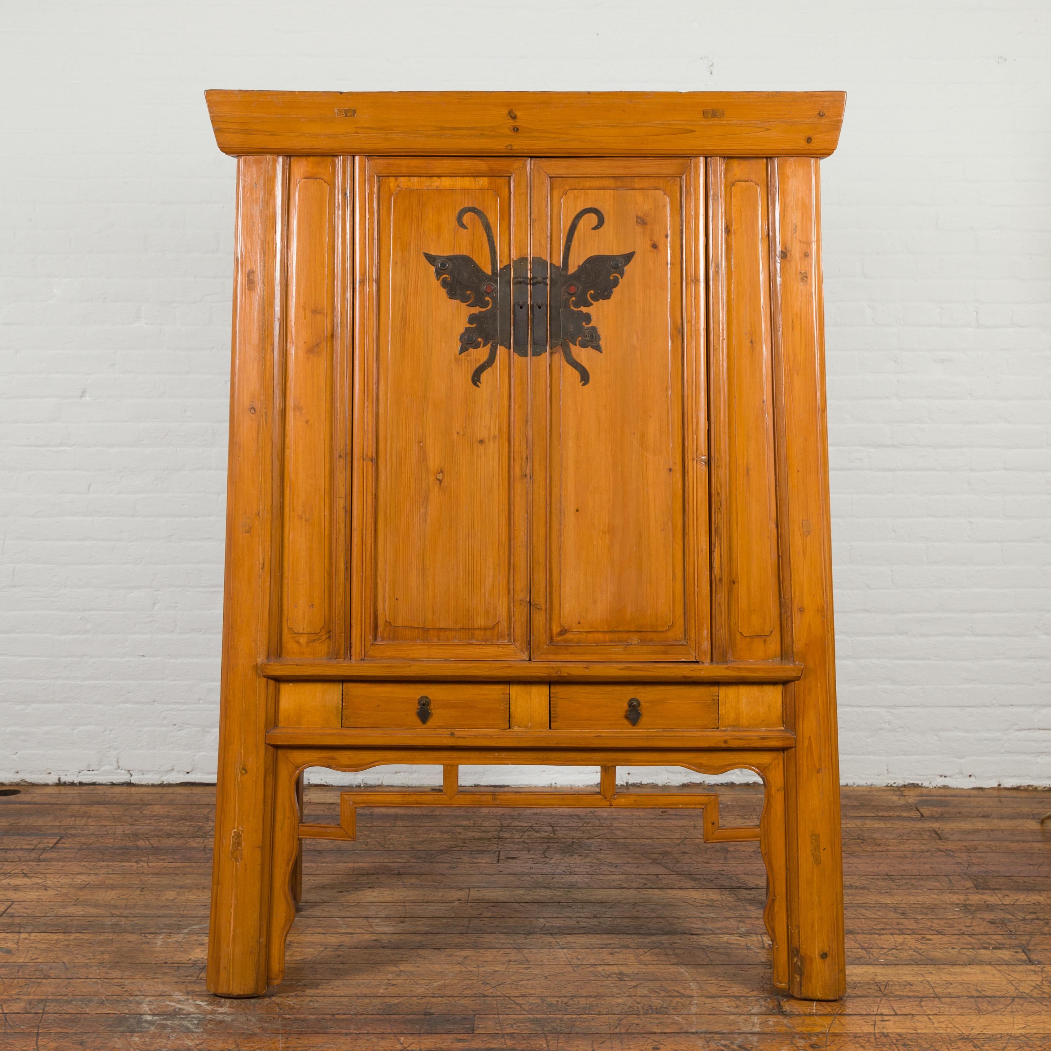 A Chinese vintage elmwood wedding cabinet from the mid 20th century, with butterfly hardware. Created in China during the midcentury period, this wedding cabinet features a beveled cornice sitting above a tapering structure. Showcasing a large