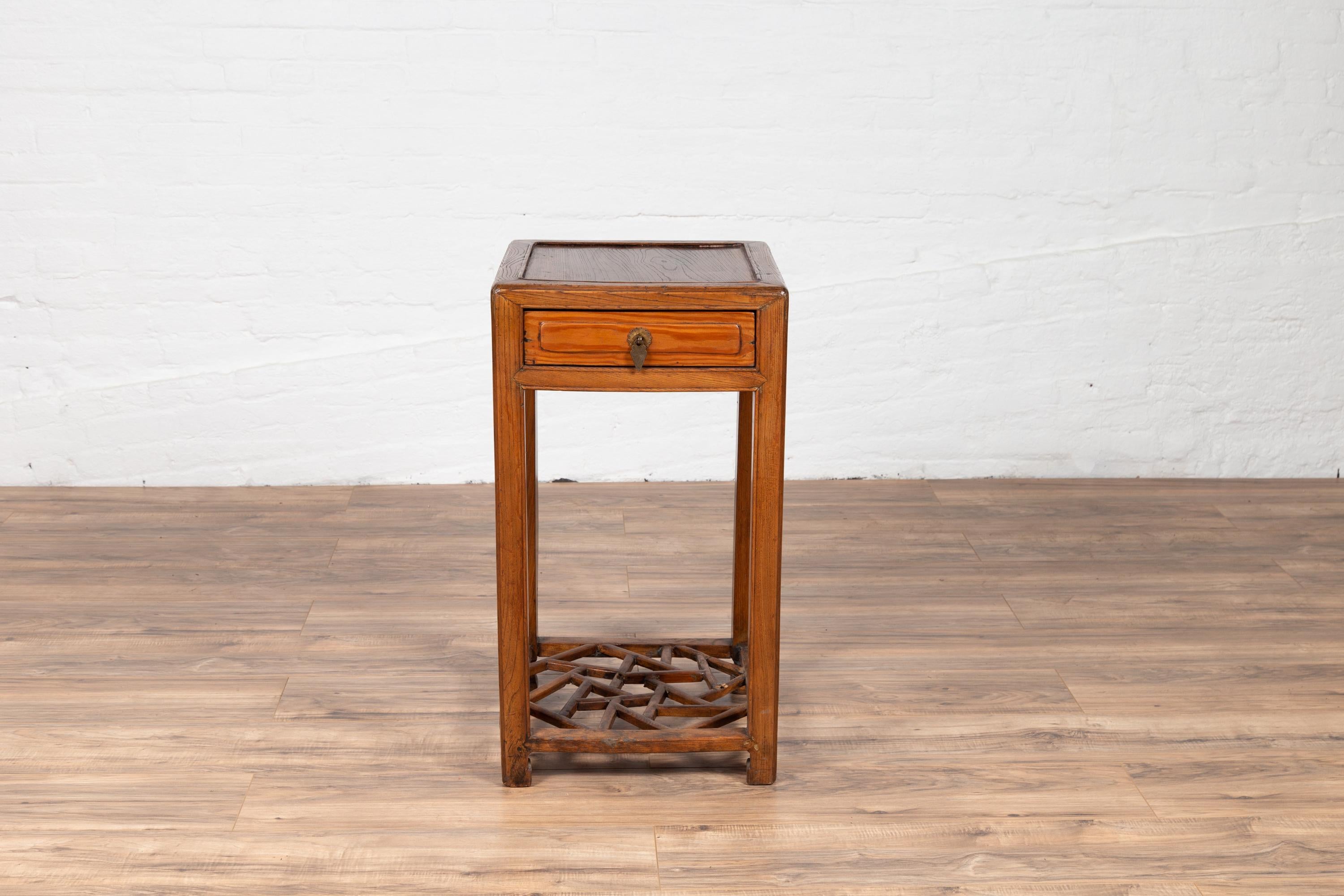 A Chinese vintage elmwood lamp table from the mid-20th century, with single drawer and cracked ice shelf. Born in China during the midcentury era, this charming side table features a square top accented with a thin molding, resting above a single