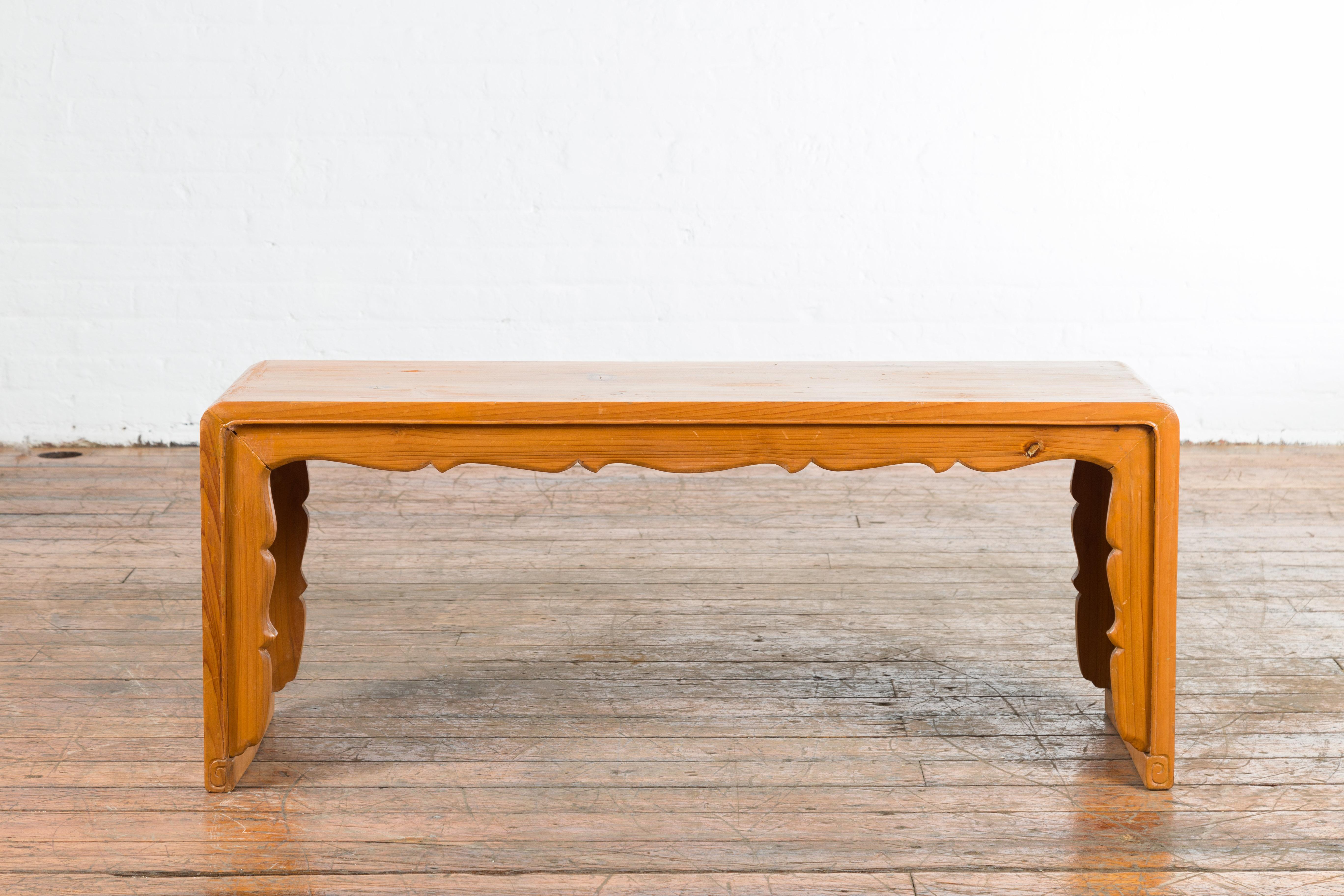 Our vintage elmwood waterfall coffee table from the mid 20th century features a beautifully carved apron that cascades down the side legs of the vintage coffee table. The waterfall design coupled with the artistically crafted carvings makes this