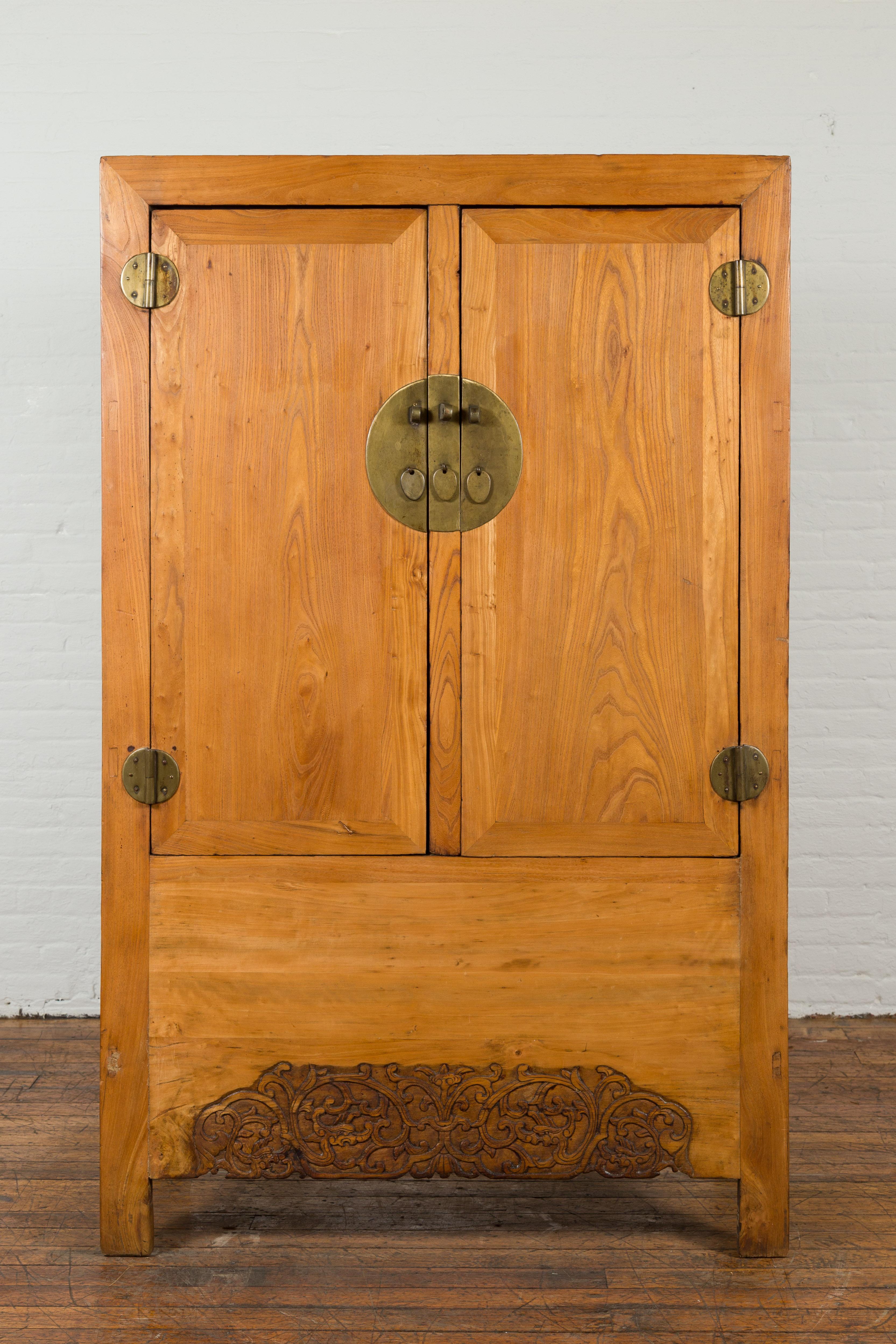 A Chinese vintage elmwood wedding cabinet from the mid 20th century with a carved lower apron, two hidden internal drawers and brass hardware. Featured in our vast cabinets collection, we currently have have two of these large vintage cabinets