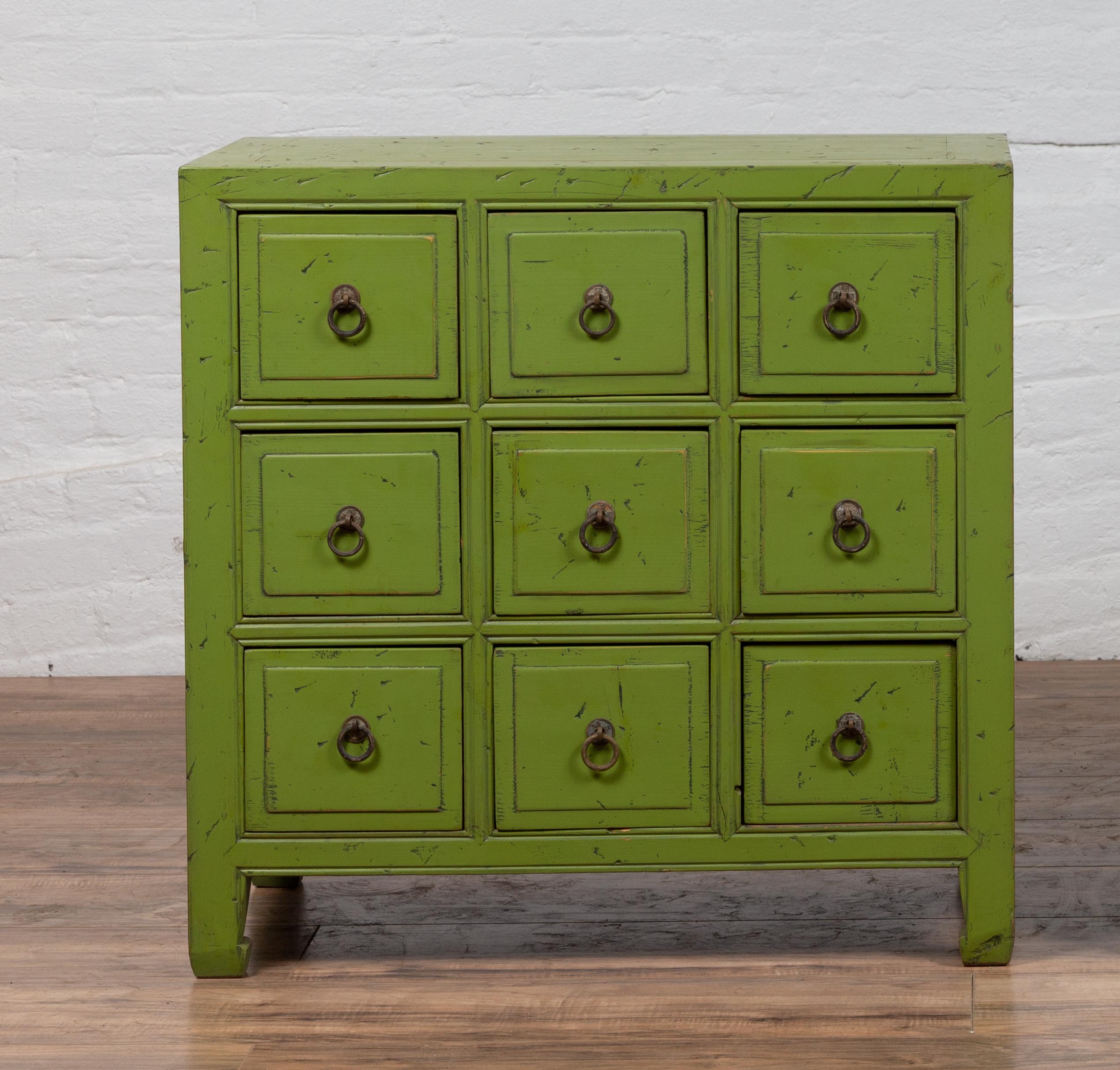 A Chinese vintage green painted nine-drawer apothecary bedside chest from the mid-20th century, with black splatter. Born in China during the midcentury period, this charming apothecary chest features a rectangular top, sitting above a perfectly