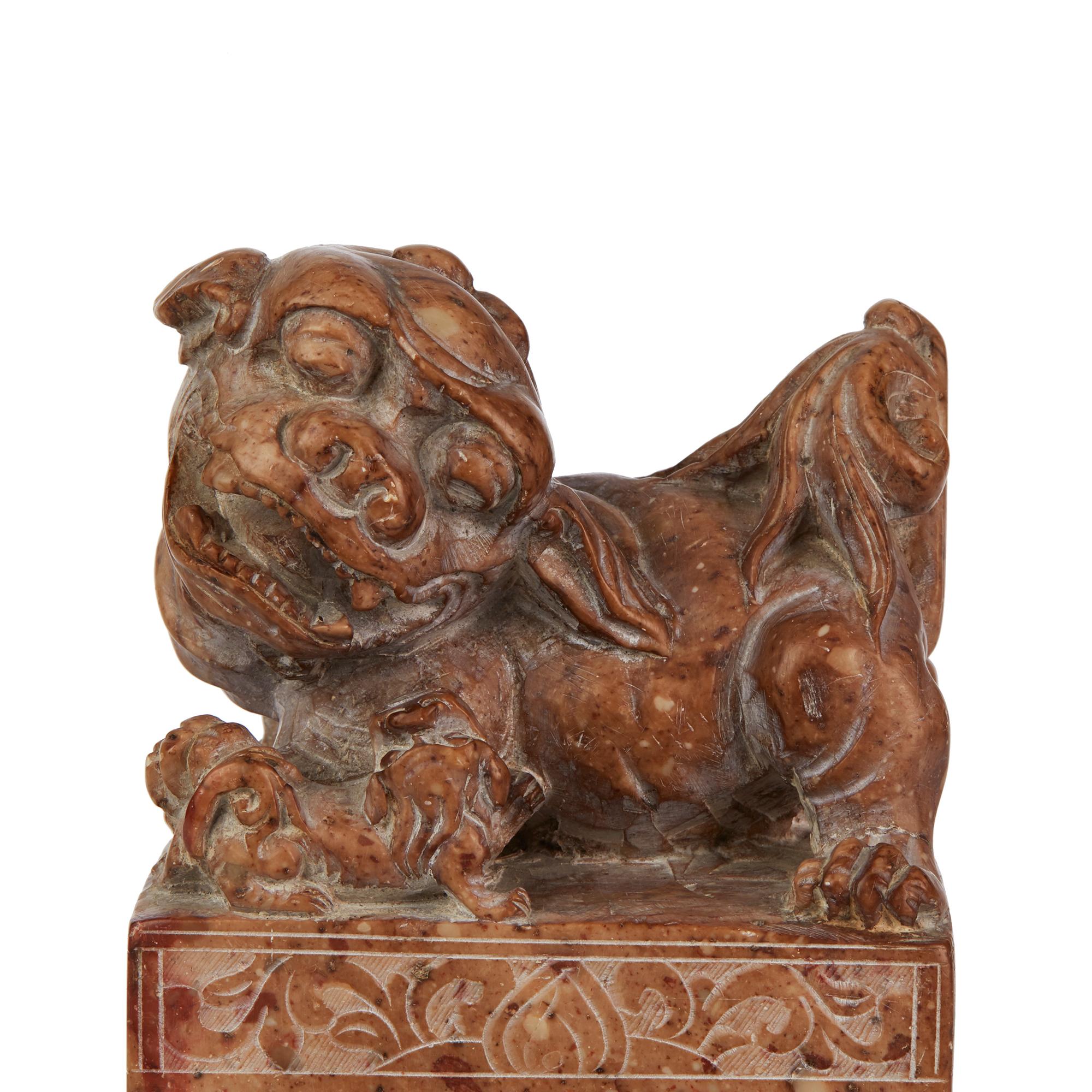 A large and well carved Chinese soap stone seal of rectangular form carved with a large dog of Fo and puppy to the top. Carved in a brown and slight rose coloured stone the body of the seal is carved with floral panels, the front with a vessel