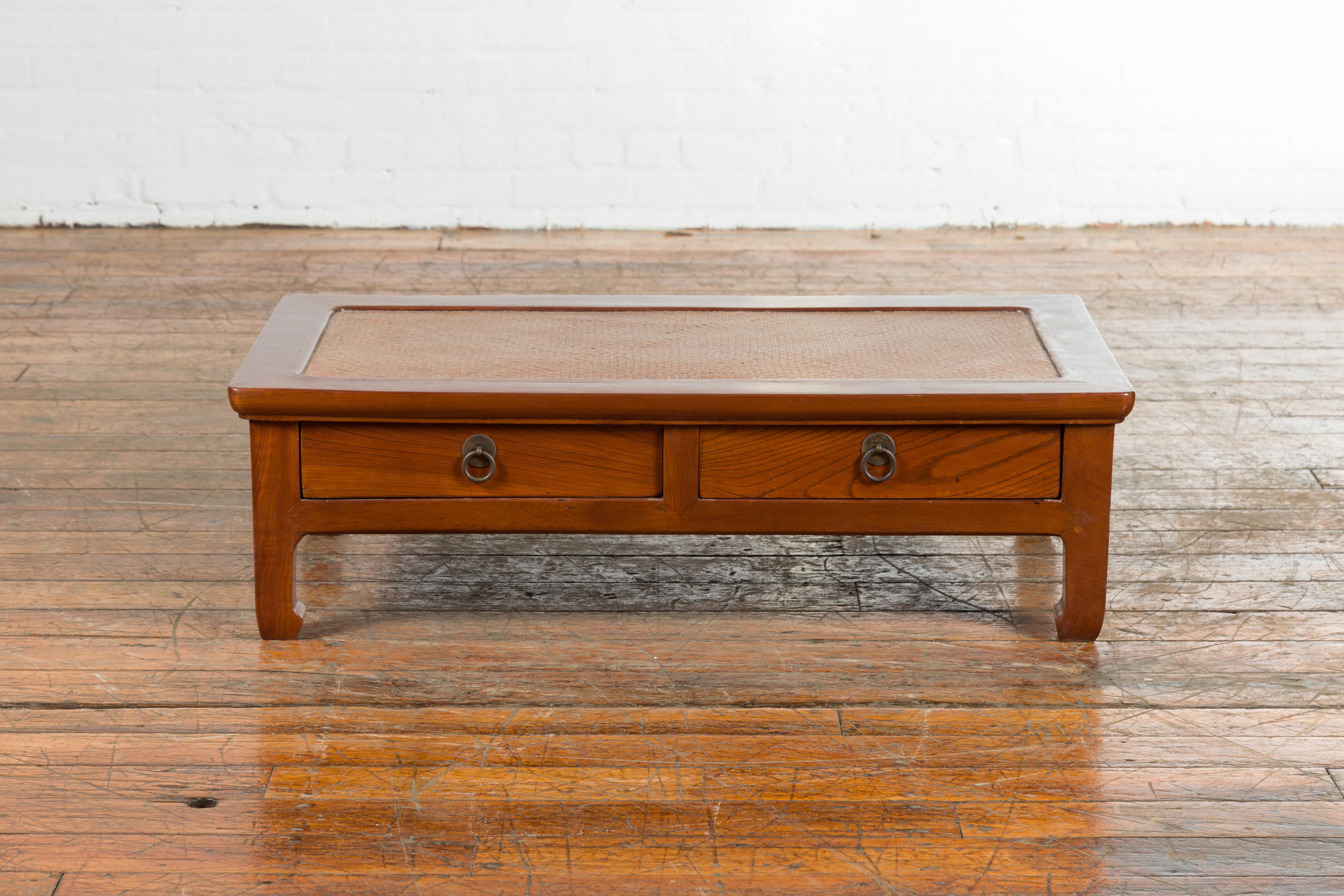 A Chinese vintage low elmwood table from the mid 20th century, with rattan inset top, two drawers and horsehoof feet. Created in China during the midcentury period, this low elm table features a rectangular top with rattan insert, sitting above two