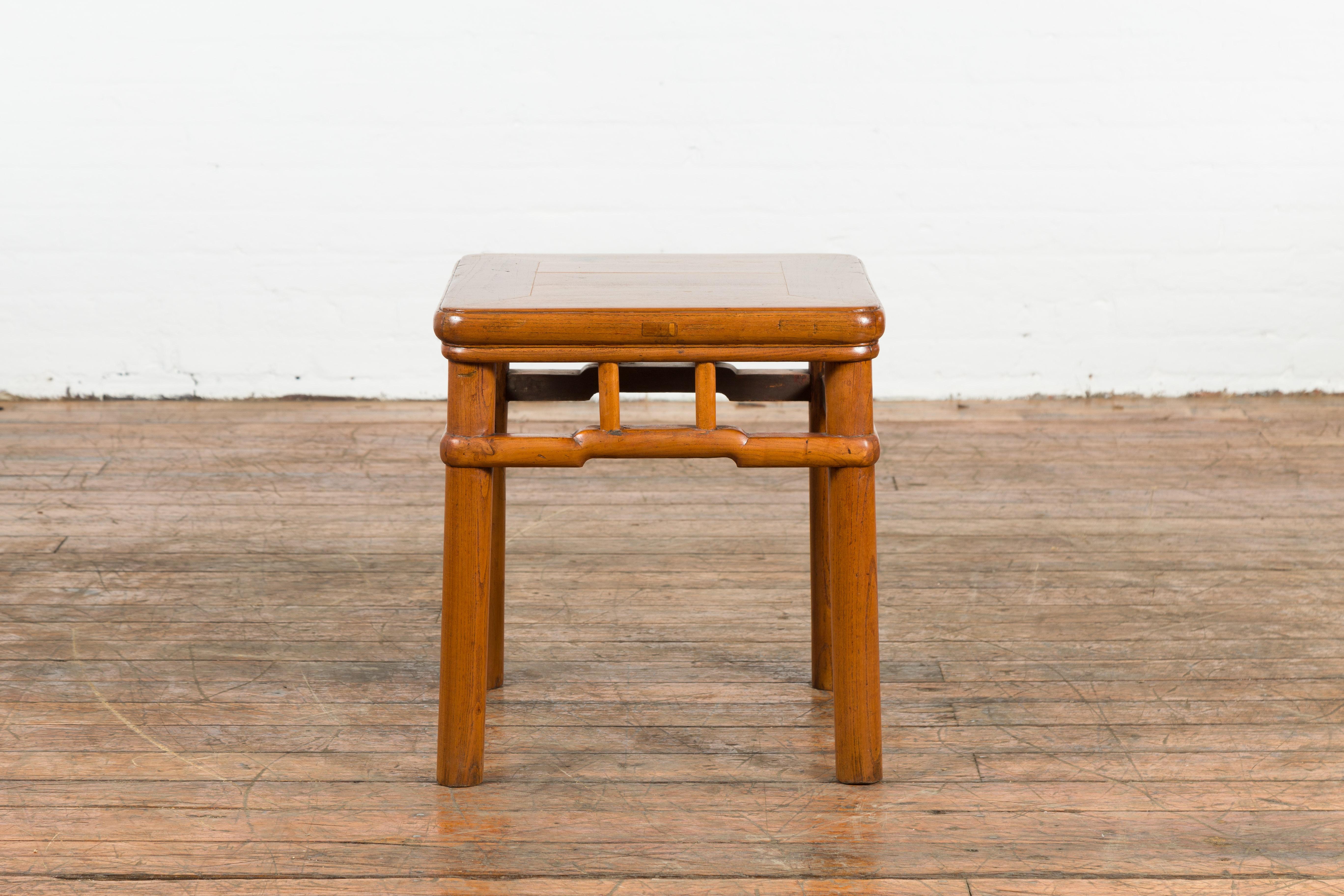 A Chinese vintage side table from the mid 20th century, with humpback stretcher, pierced apron and light brown lacquer. Created in China during the midcentury period, this Chinese side table features a square top with central board, sitting above a